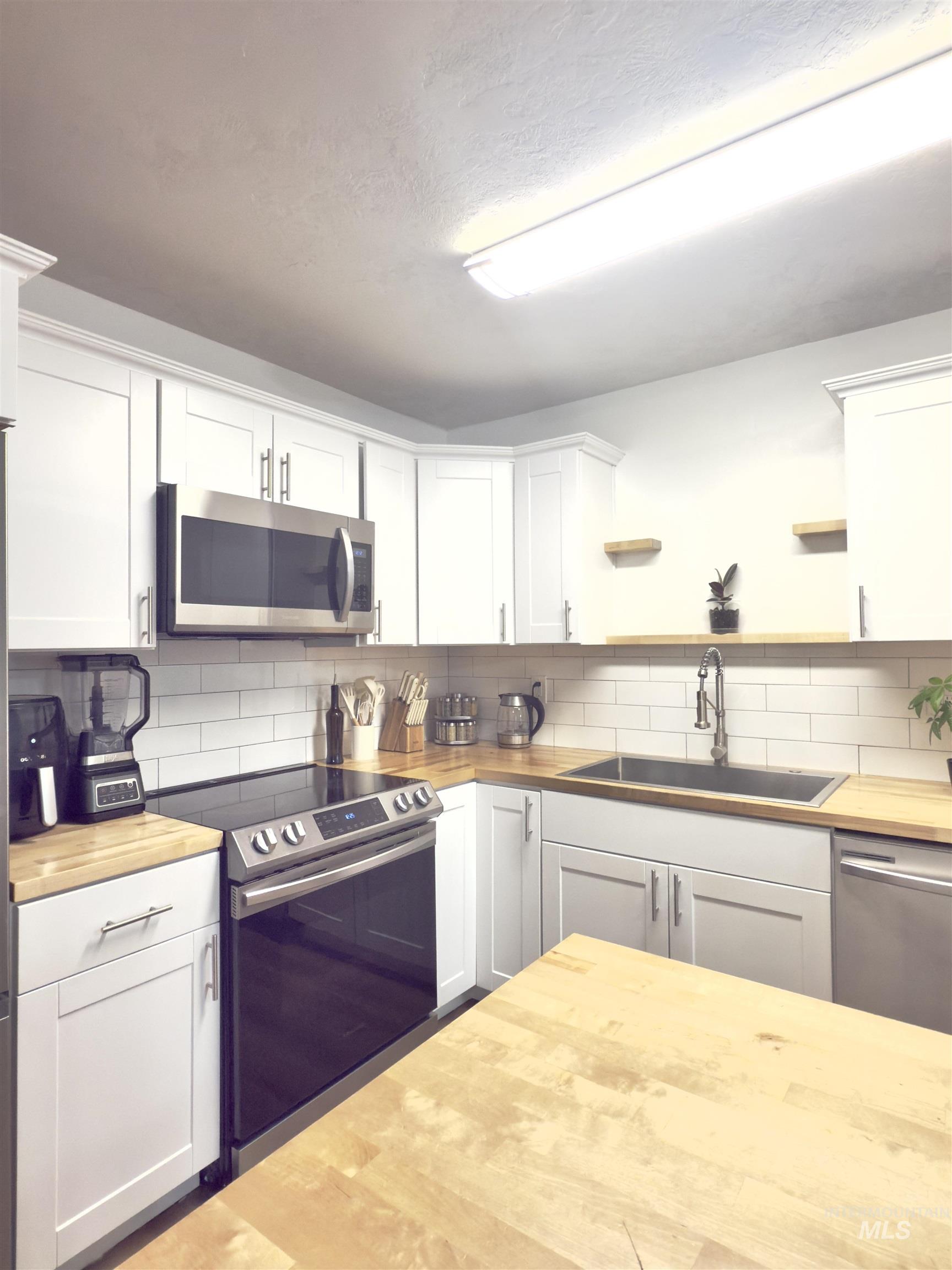 Kitchen featuring stainless steel appliances, white cabinetry, butcher block countertops, tasteful backsplash, and a textured ceiling