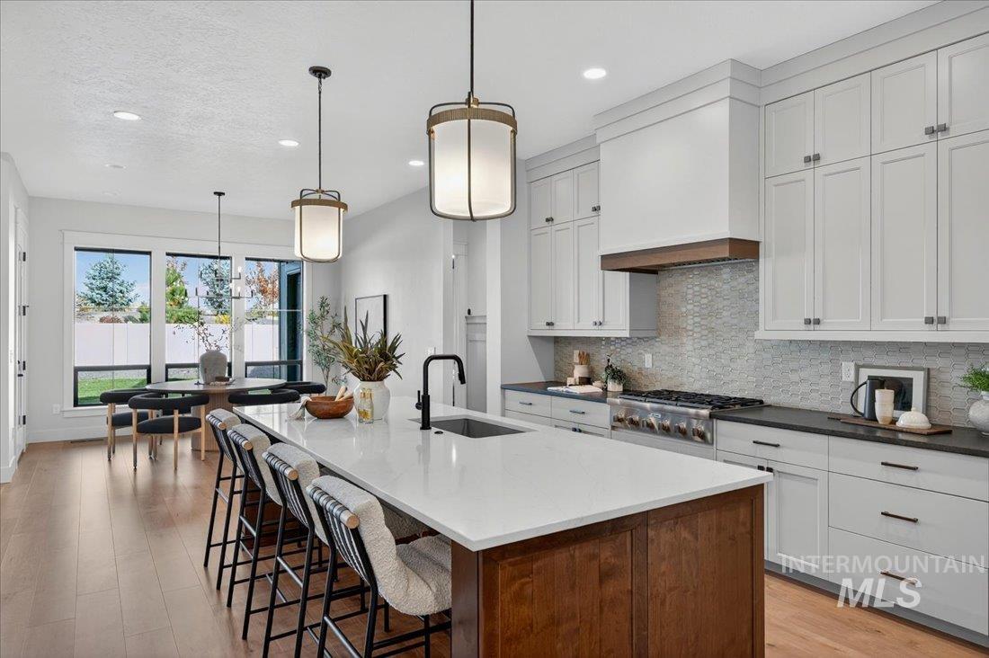 Kitchen with decorative backsplash, light wood-style flooring, a breakfast bar, a kitchen island with sink, and white cabinetry