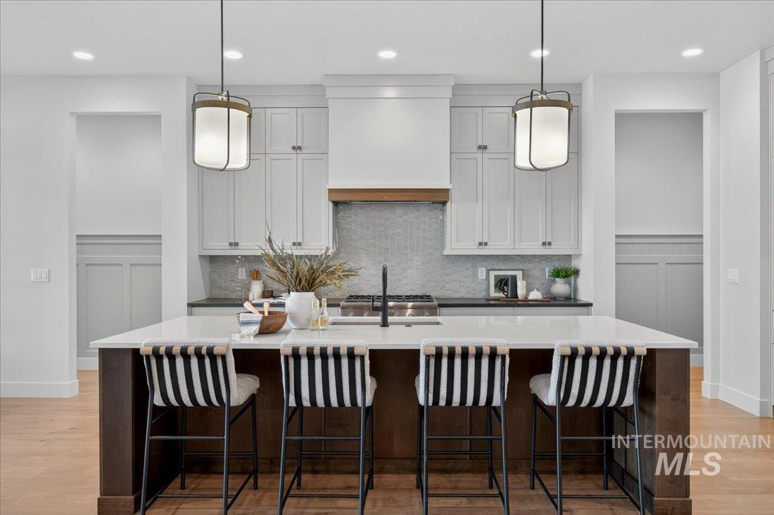Kitchen with backsplash, light wood-style floors, white cabinetry, a kitchen bar, and pendant lighting