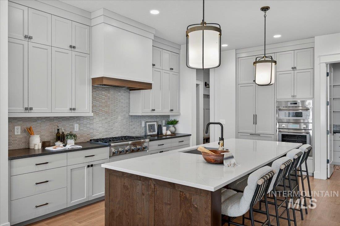 Kitchen featuring a breakfast bar, tasteful backsplash, a center island with sink, light wood-style floors, and white cabinetry