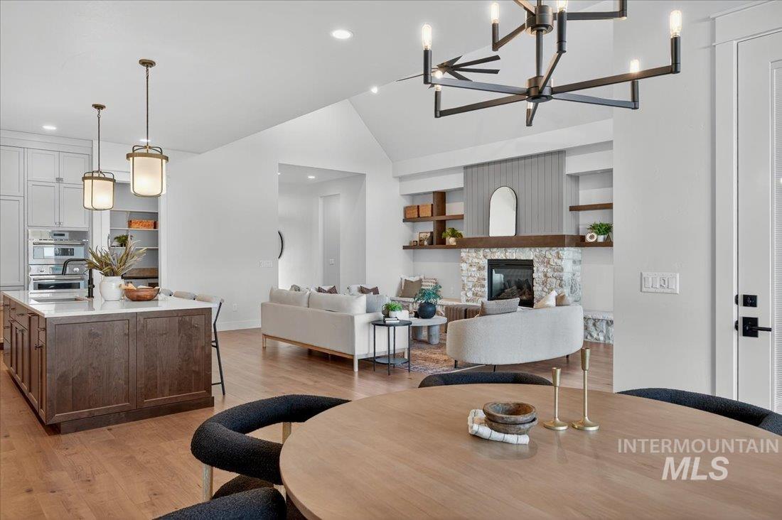 Dining area featuring lofted ceiling, light wood-type flooring, a stone fireplace, recessed lighting, and a chandelier
