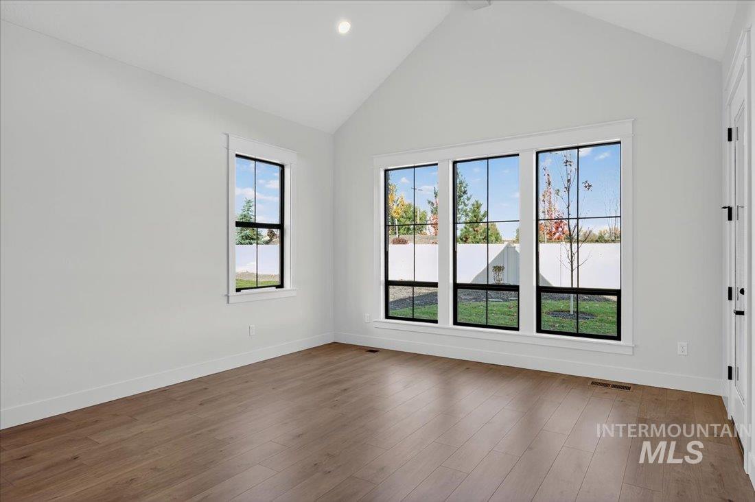 Empty room featuring wood finished floors, high vaulted ceiling, and recessed lighting