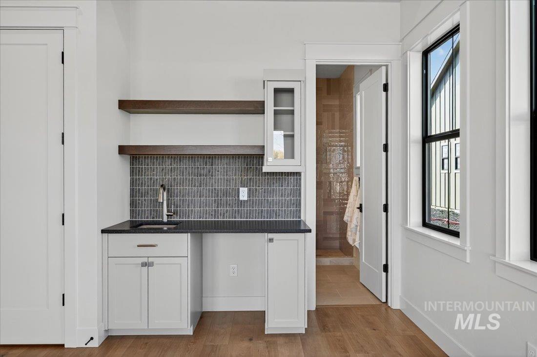 Kitchen featuring white cabinetry, open shelves, backsplash, light wood finished floors, and glass insert cabinets