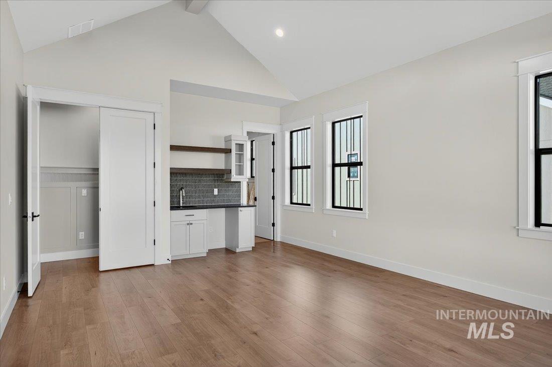 Unfurnished living room with light wood finished floors, beamed ceiling, and high vaulted ceiling