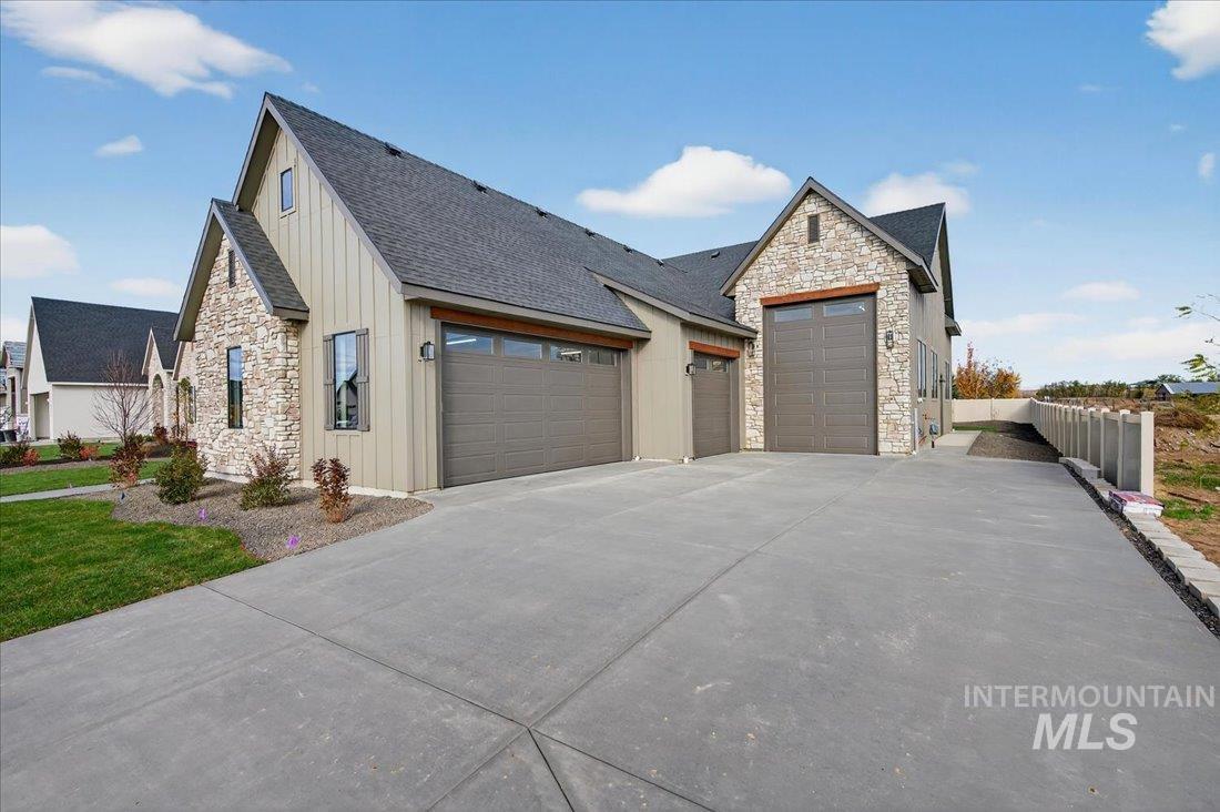 View of front of property with stone siding, board and batten siding, driveway, a garage, and a shingled roof