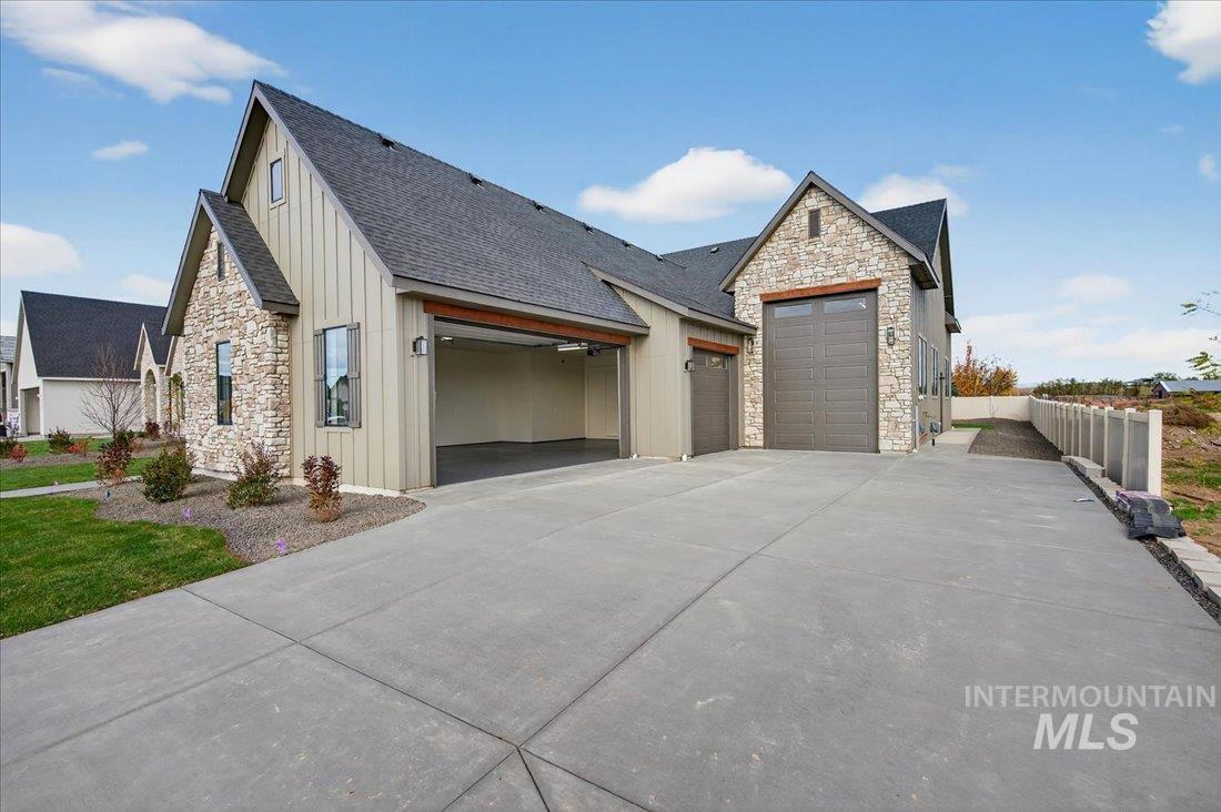 View of front of house featuring board and batten siding, stone siding, a garage, concrete driveway, and roof with shingles