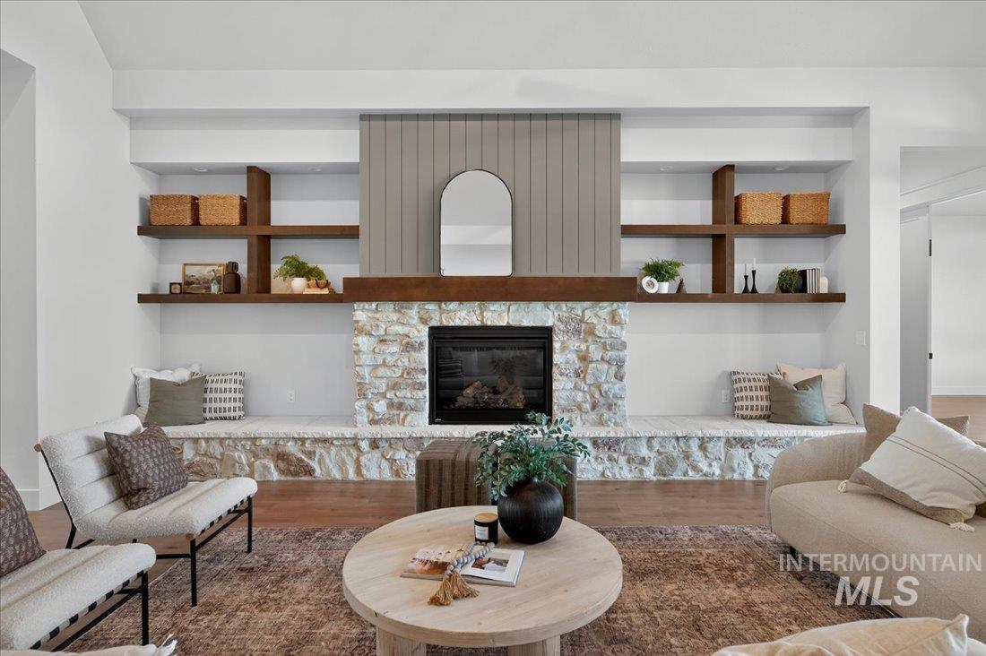 Living room with wood finished floors, a stone fireplace, and built in shelves
