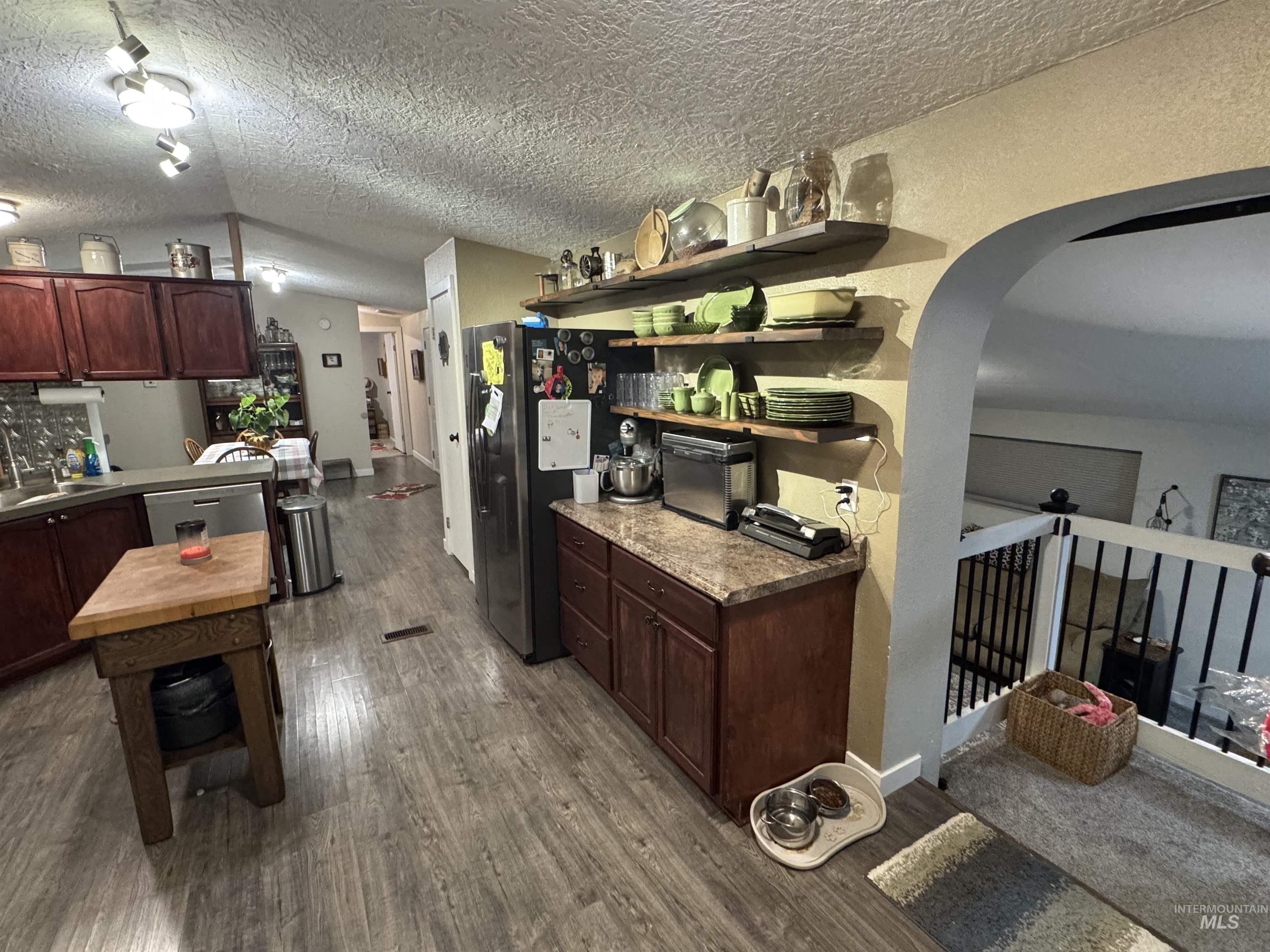 Kitchen with open shelves, dark wood-style floors, dark brown cabinets, arched walkways, and a textured ceiling