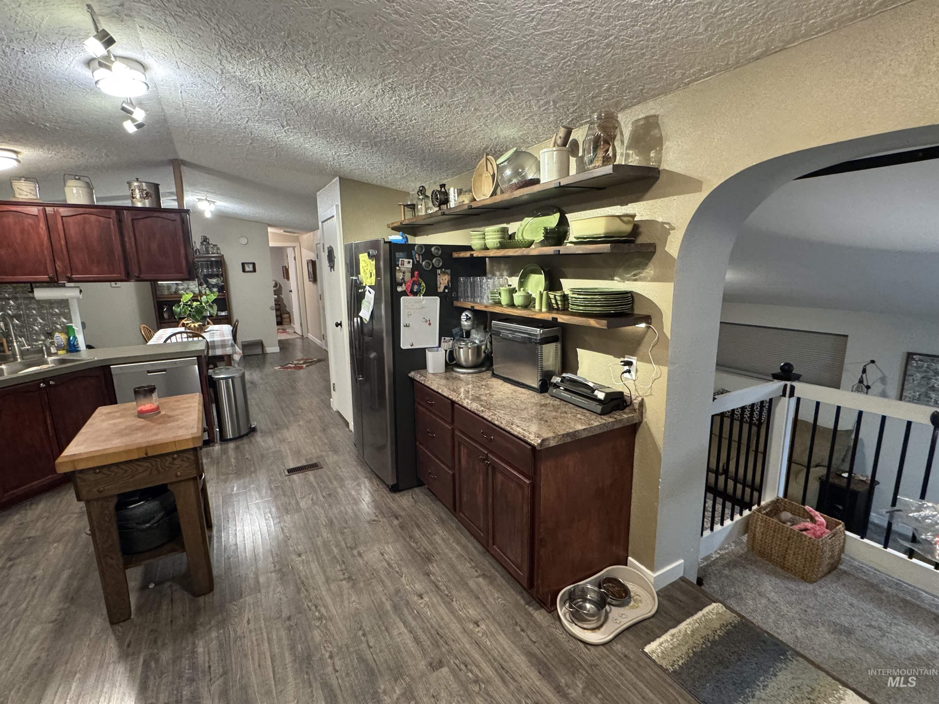 Kitchen with open shelves, dark wood-style floors, arched walkways, appliances with stainless steel finishes, and dark brown cabinetry