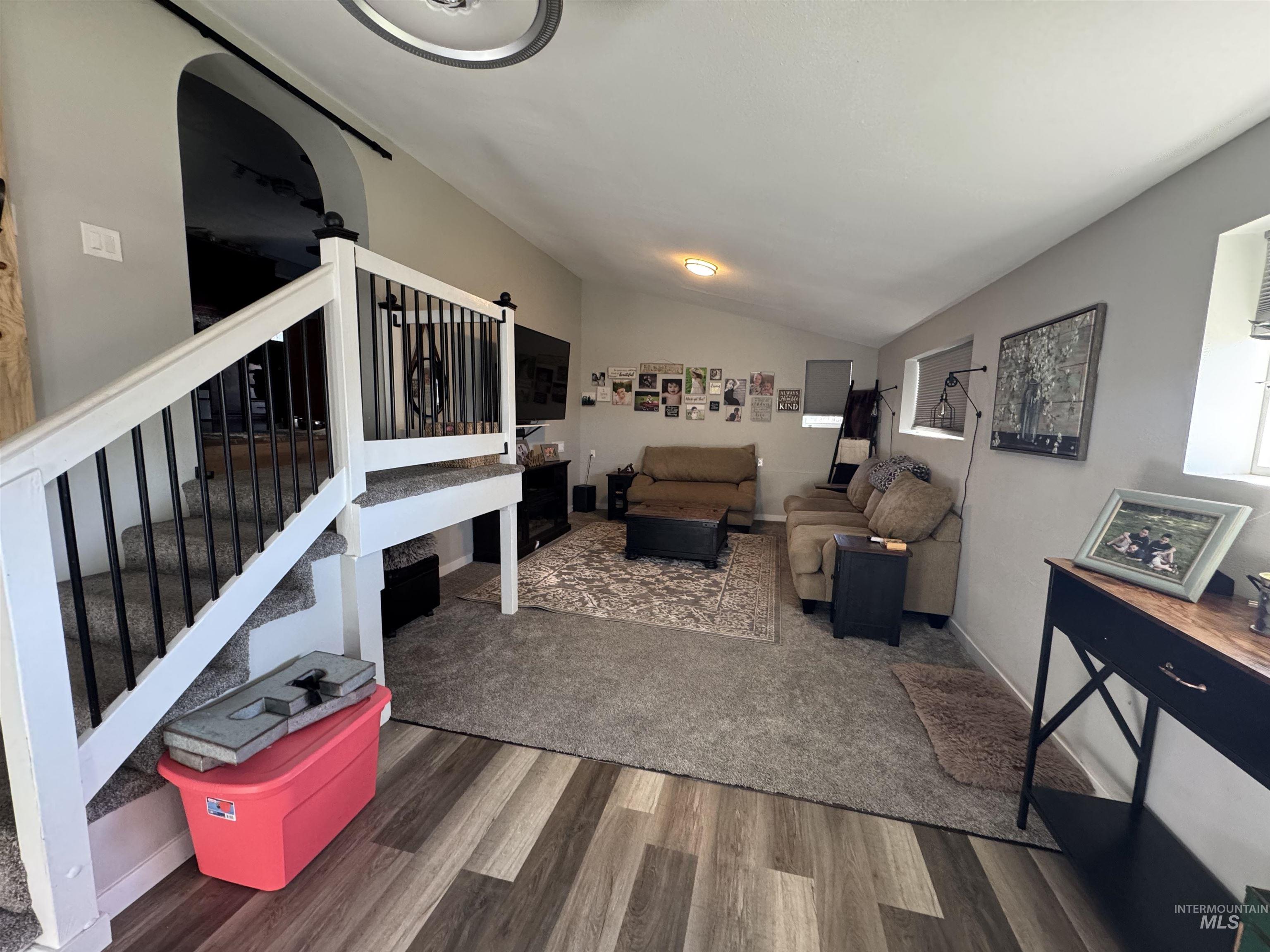 Living area featuring stairway, lofted ceiling, wood finished floors, and arched walkways