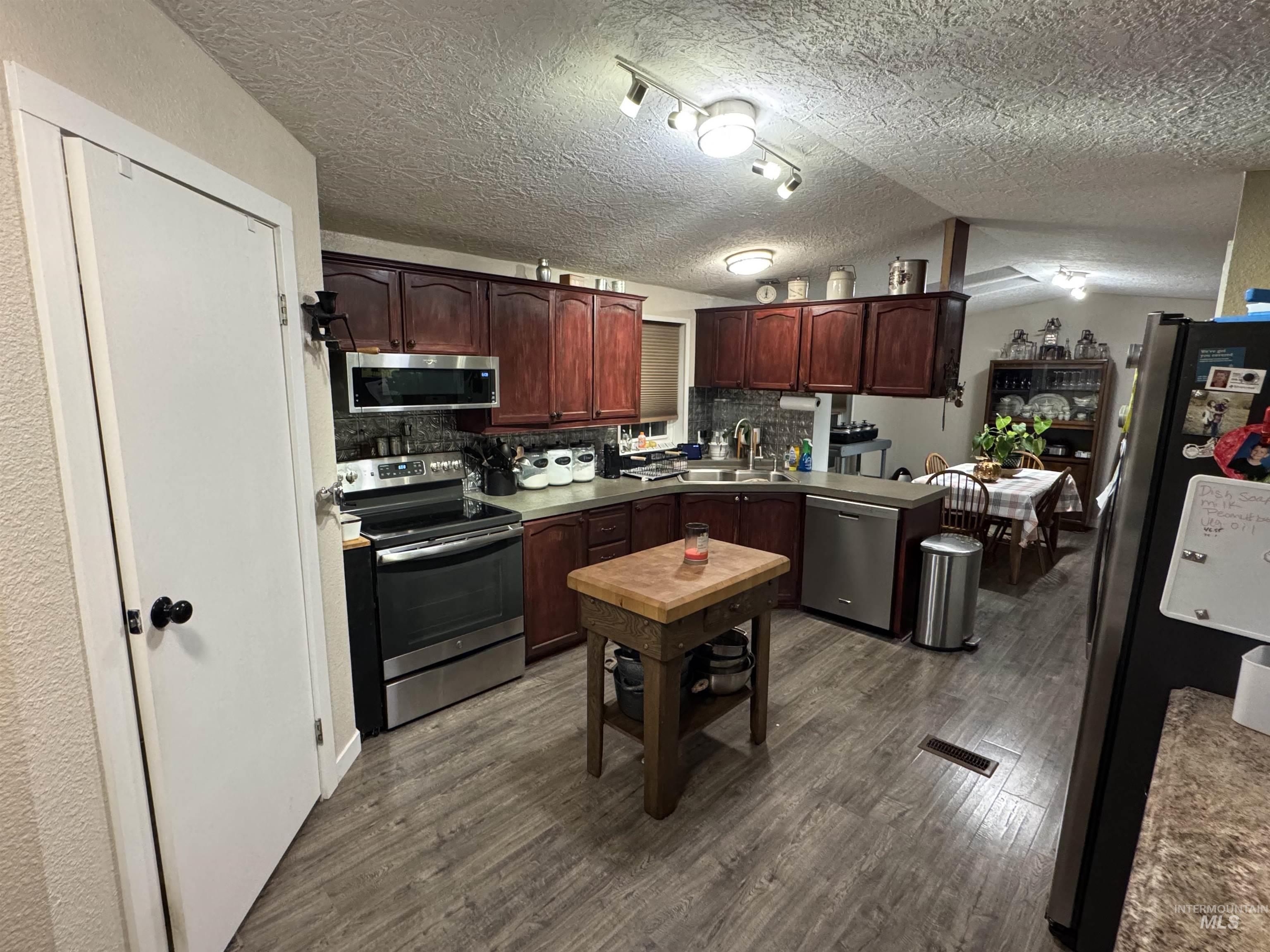 Kitchen featuring appliances with stainless steel finishes, dark wood finished floors, tasteful backsplash, a textured ceiling, and light countertops