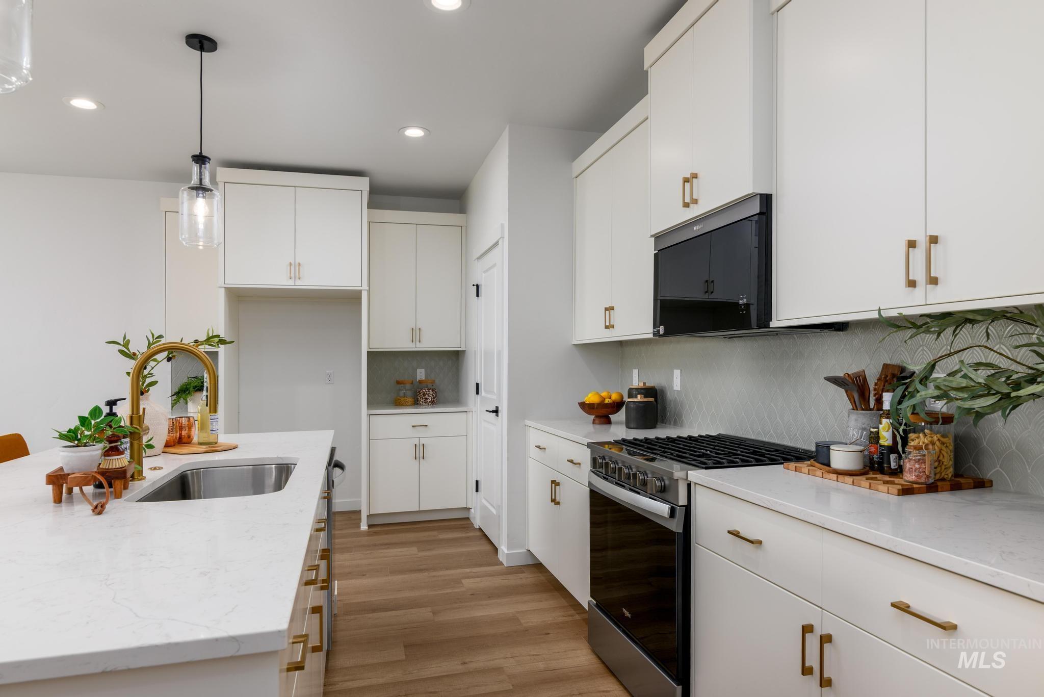 Kitchen with hanging light fixtures, stainless steel gas stove, white cabinets, backsplash, and recessed lighting