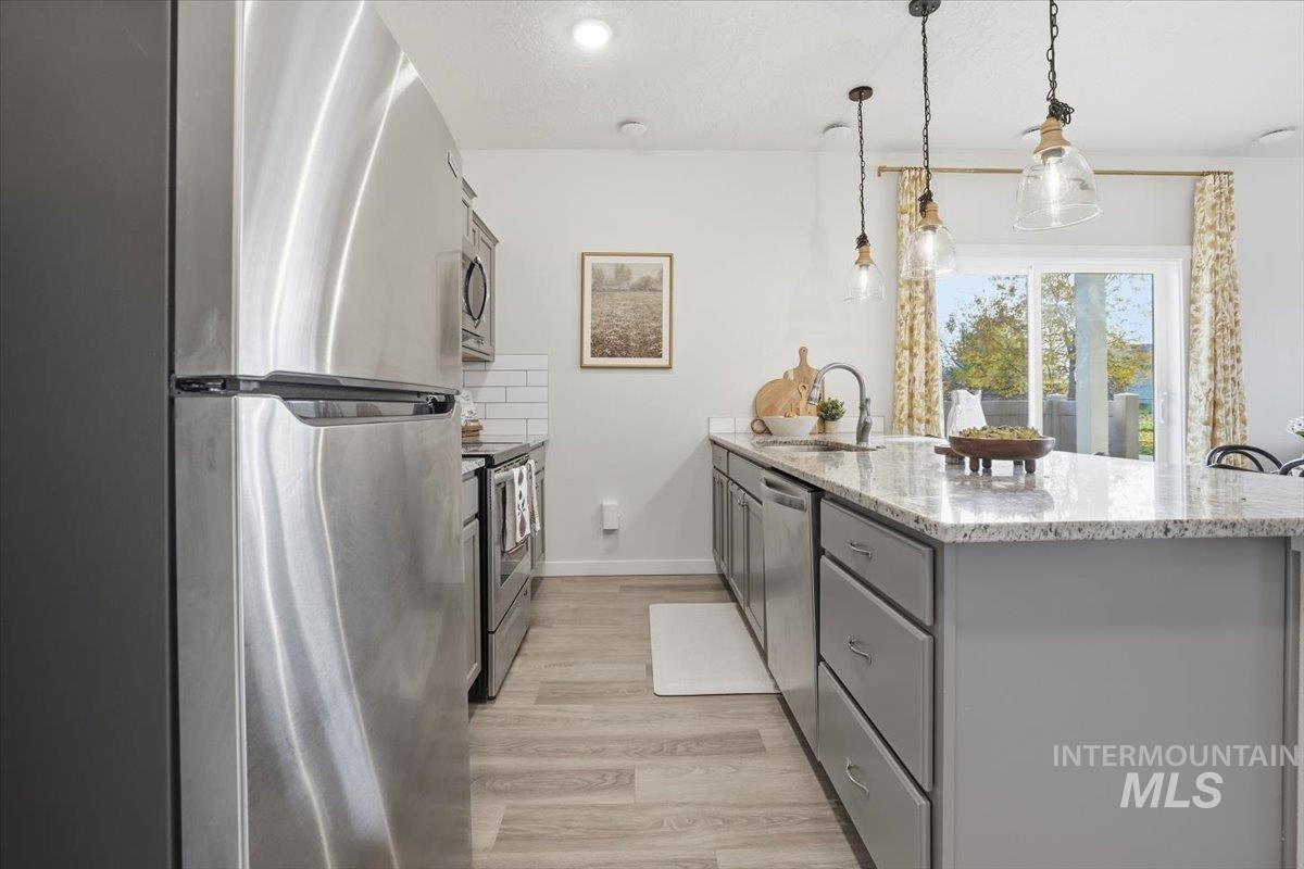 Kitchen with stainless steel appliances, light wood finished floors, light stone counters, a peninsula, and pendant lighting