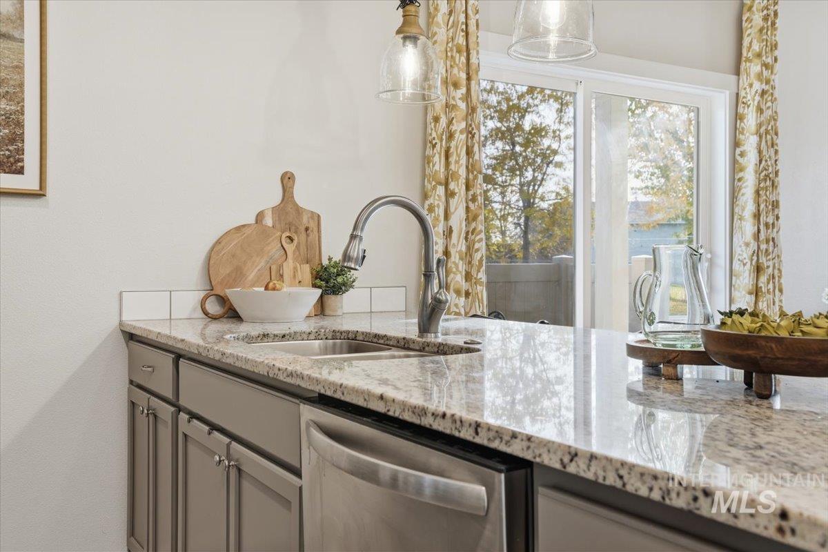 Bar area featuring gray cabinetry, light stone countertops, dishwasher, and hanging light fixtures
