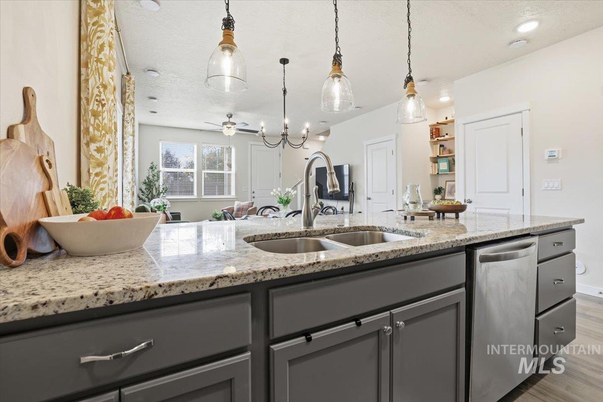 Kitchen with gray cabinetry, light stone countertops, stainless steel dishwasher, open floor plan, and hanging light fixtures