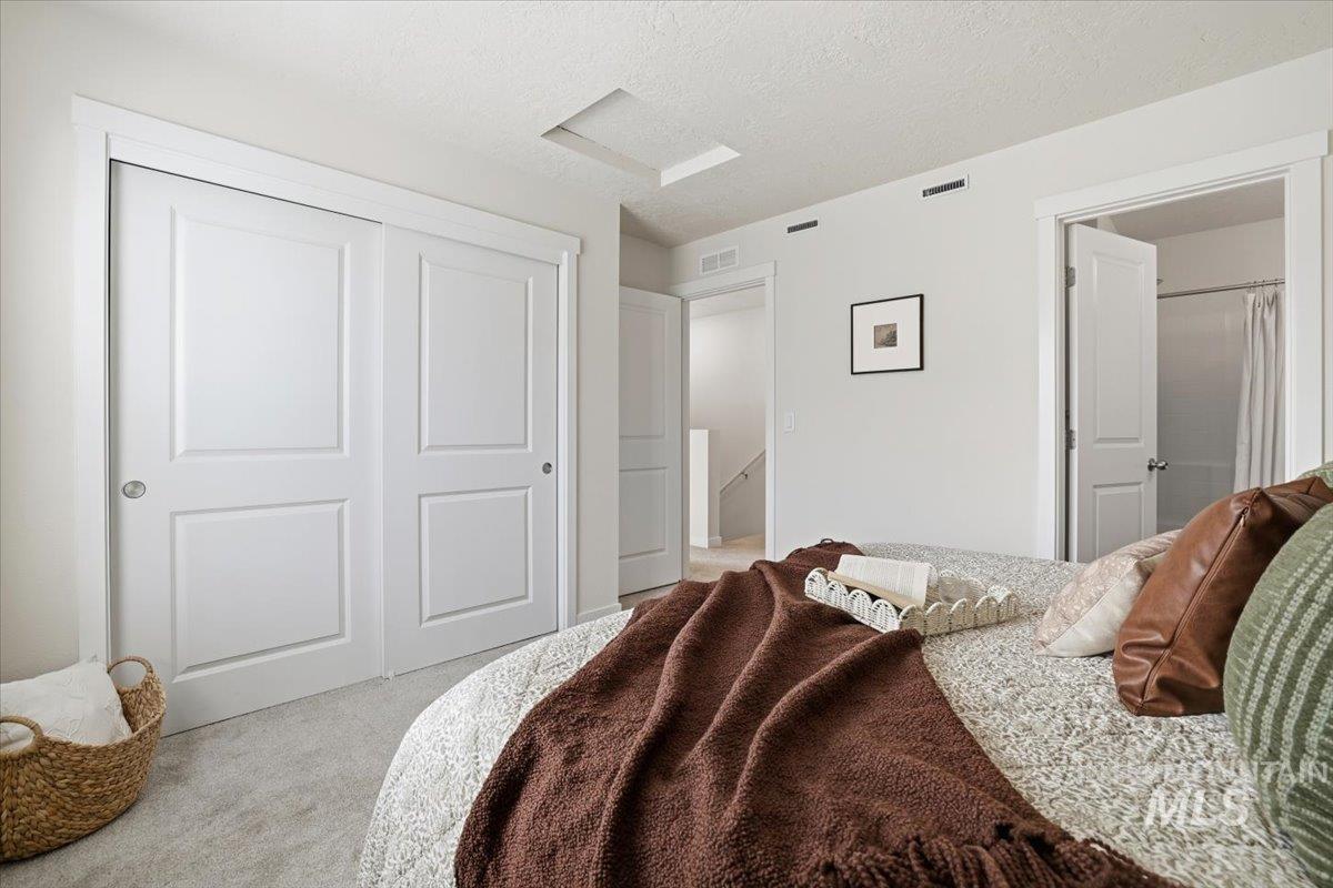 Bedroom featuring light carpet, a textured ceiling, attic access, and a closet