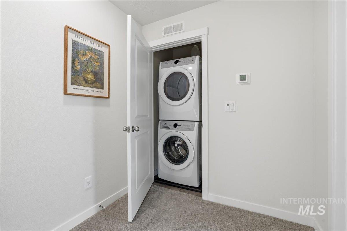 Laundry room with stacked washing machine and dryer and light carpet