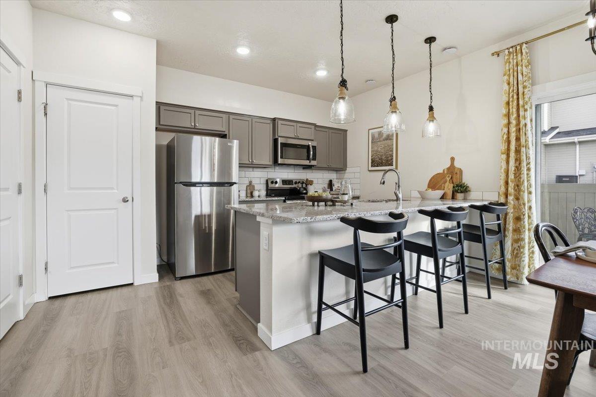 Kitchen featuring appliances with stainless steel finishes, light wood-type flooring, a breakfast bar area, decorative backsplash, and light stone counters