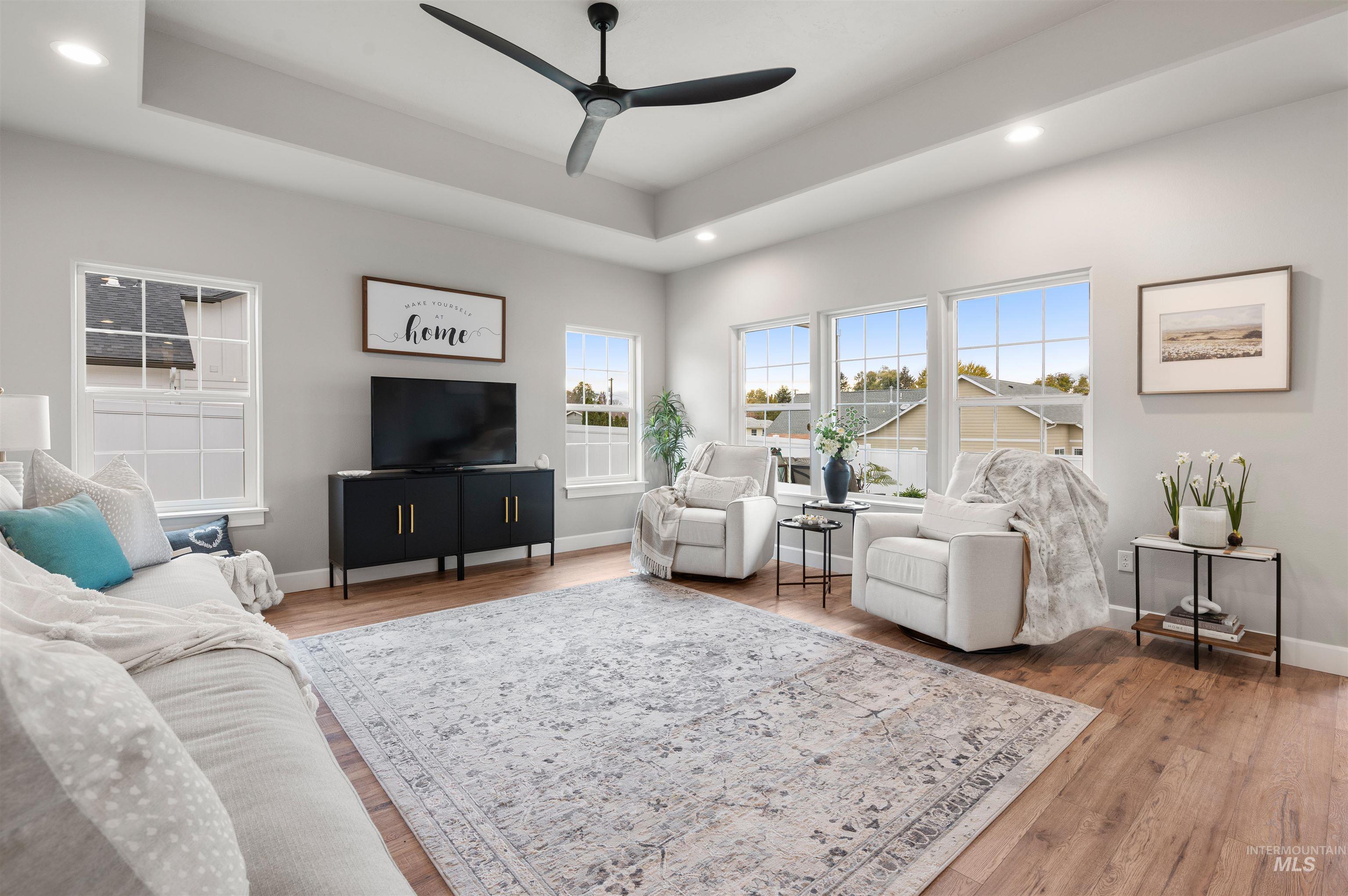Living room with a tray ceiling, recessed lighting, light wood finished floors, and a ceiling fan