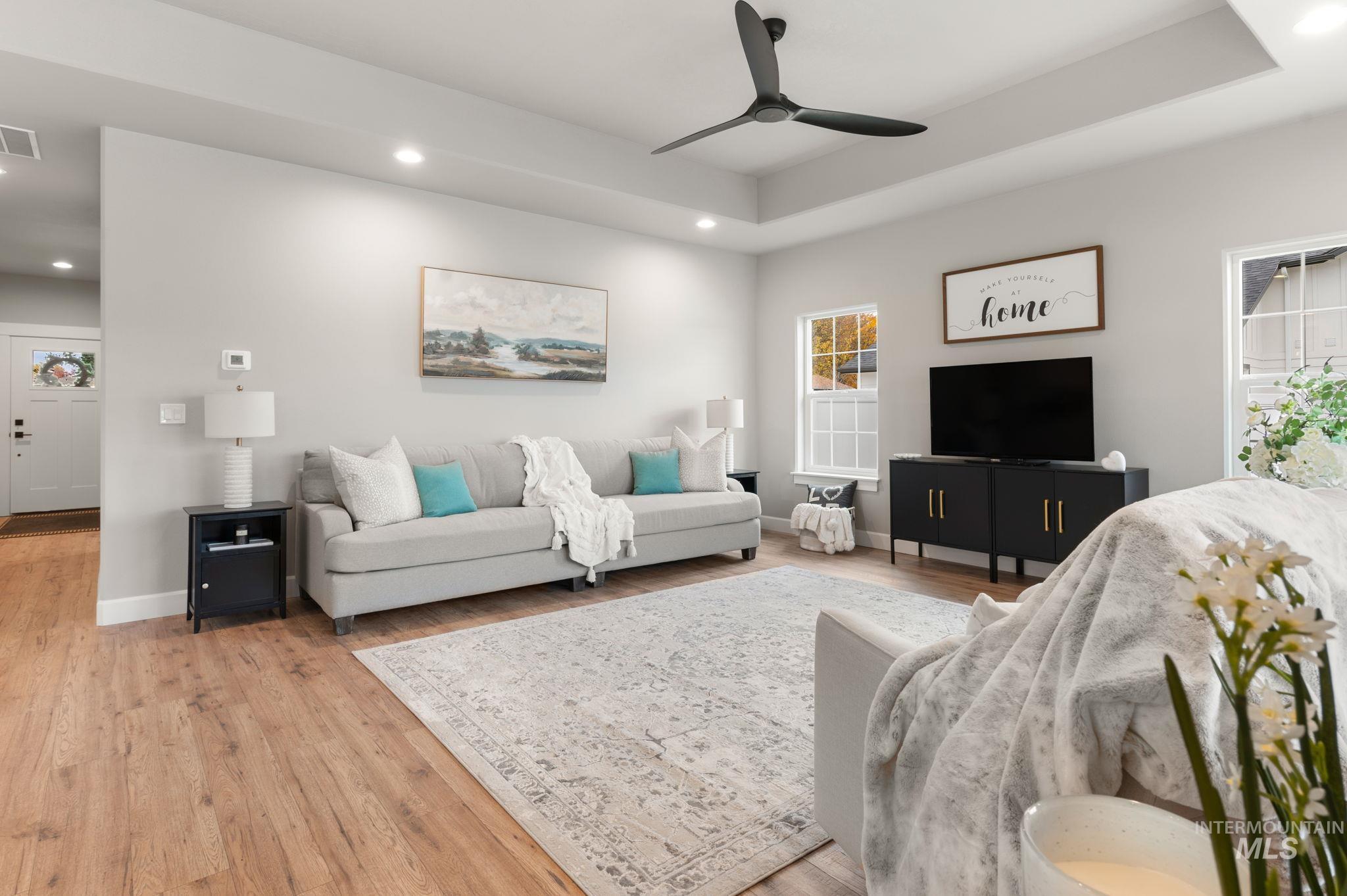 Living area with light wood-style floors, a tray ceiling, recessed lighting, and ceiling fan