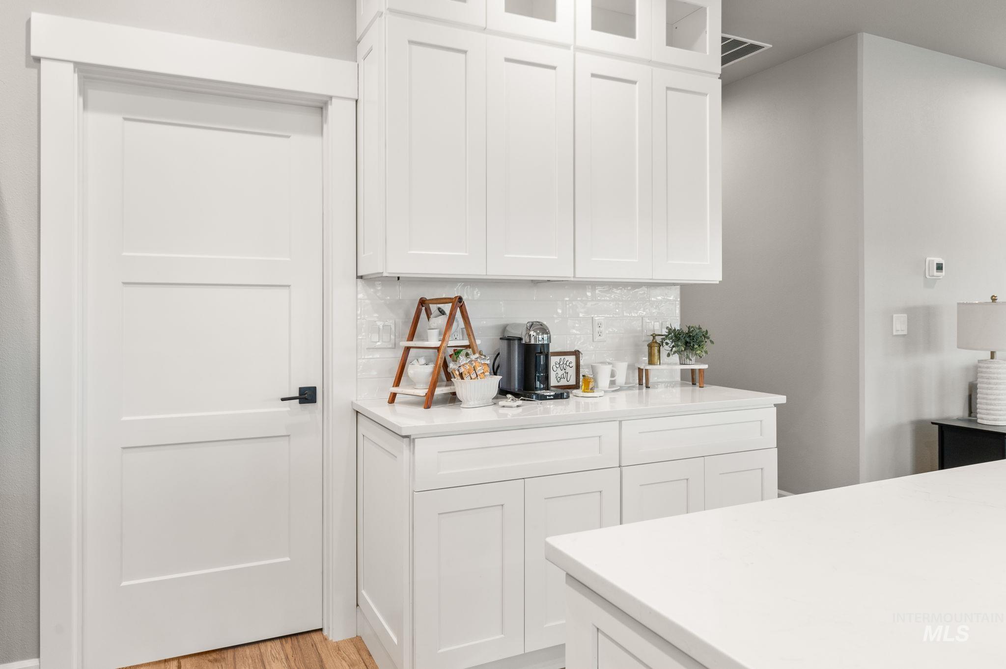 Kitchen featuring backsplash, white soft close cabinets, glass insert cabinets with lights, luxury vinyl fwood-style floors, and premium quartz counters