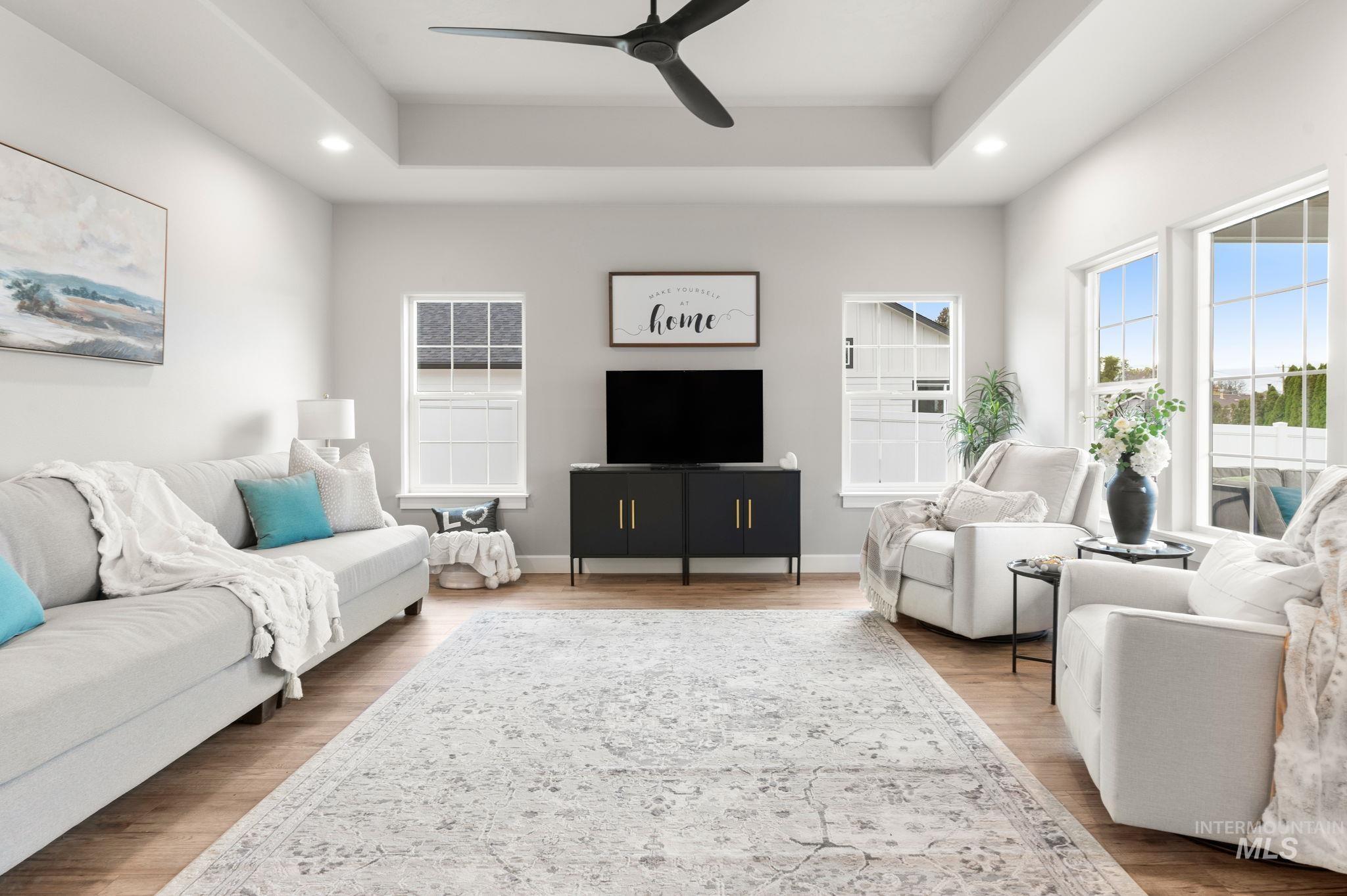 Living area featuring a raised ceiling, a ceiling fan, wood finished floors, and recessed lighting