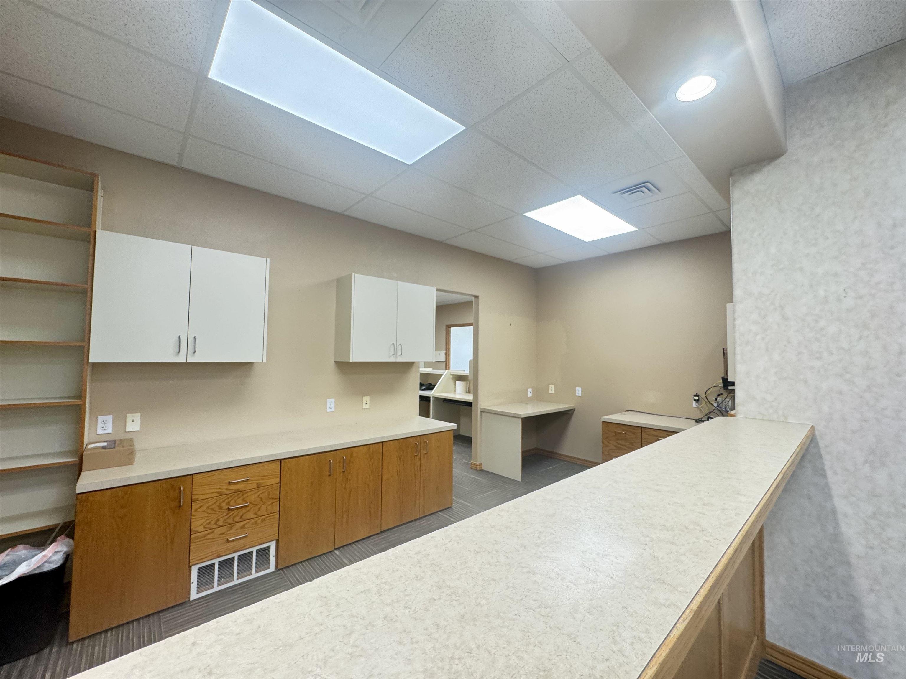 Kitchen with brown cabinets, light countertops, white cabinetry, a drop ceiling, and open shelves