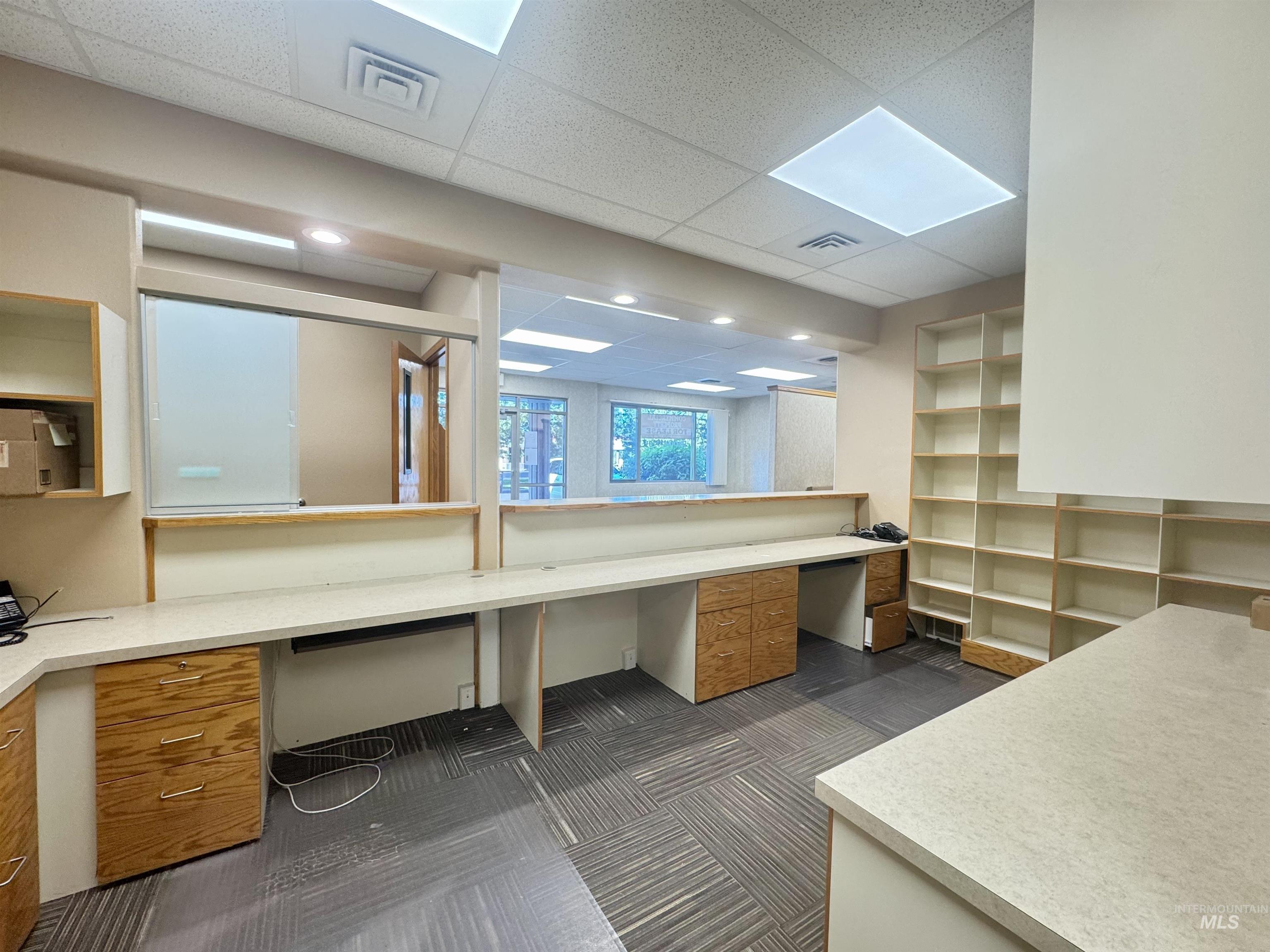 Unfurnished office with built in desk, a drop ceiling, dark carpet, and recessed lighting