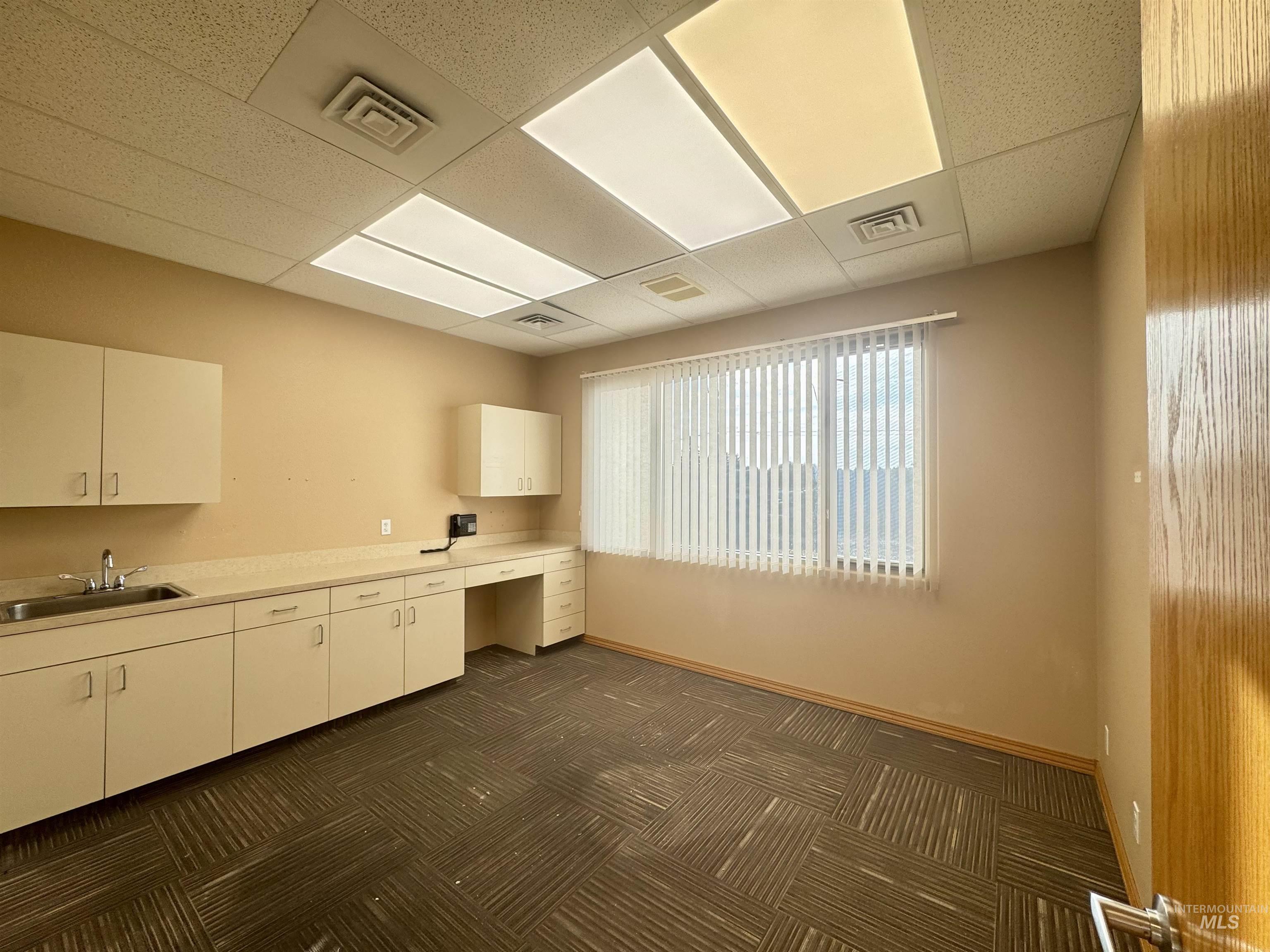 Kitchen featuring light countertops, a paneled ceiling, white cabinetry, and built in desk