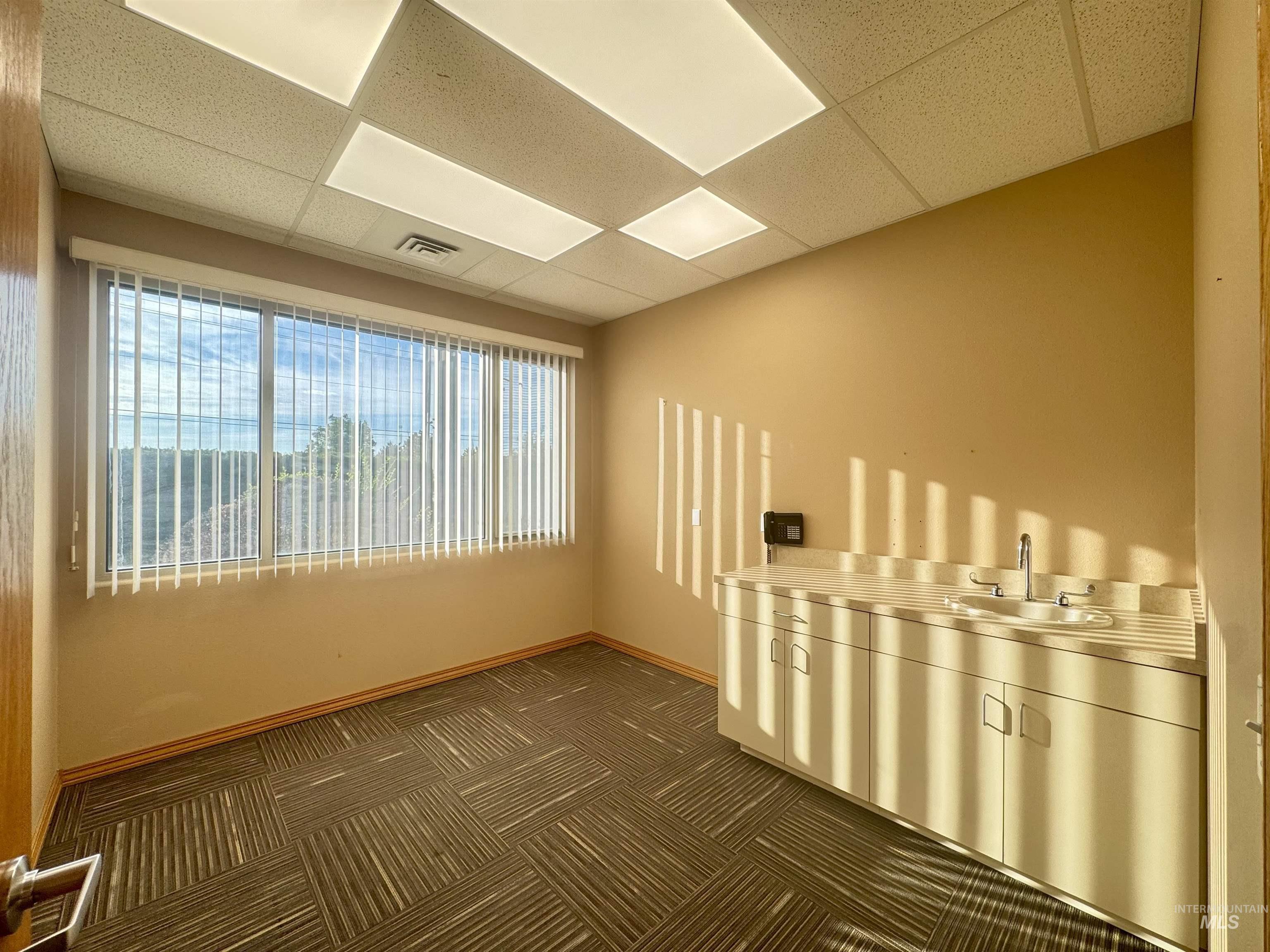 Empty room with a drop ceiling and dark colored carpet