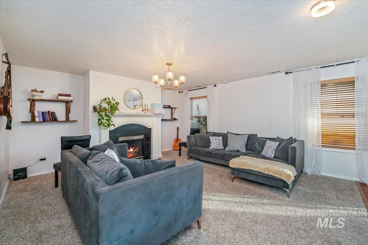 Carpeted living room featuring a textured ceiling, a tile fireplace, and a chandelier
