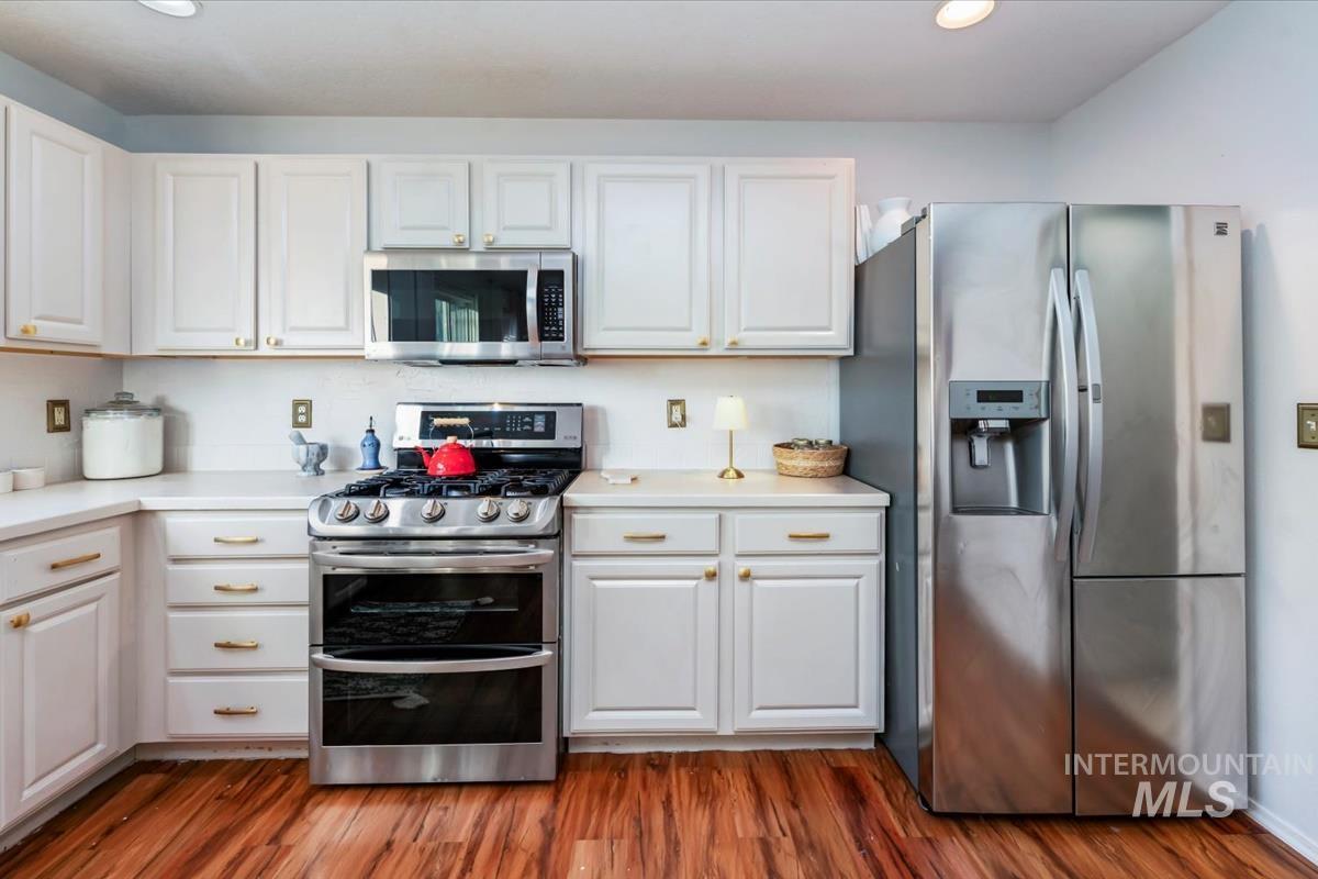 Kitchen with stainless steel appliances, white cabinets, light countertops, dark wood-style floors, and recessed lighting