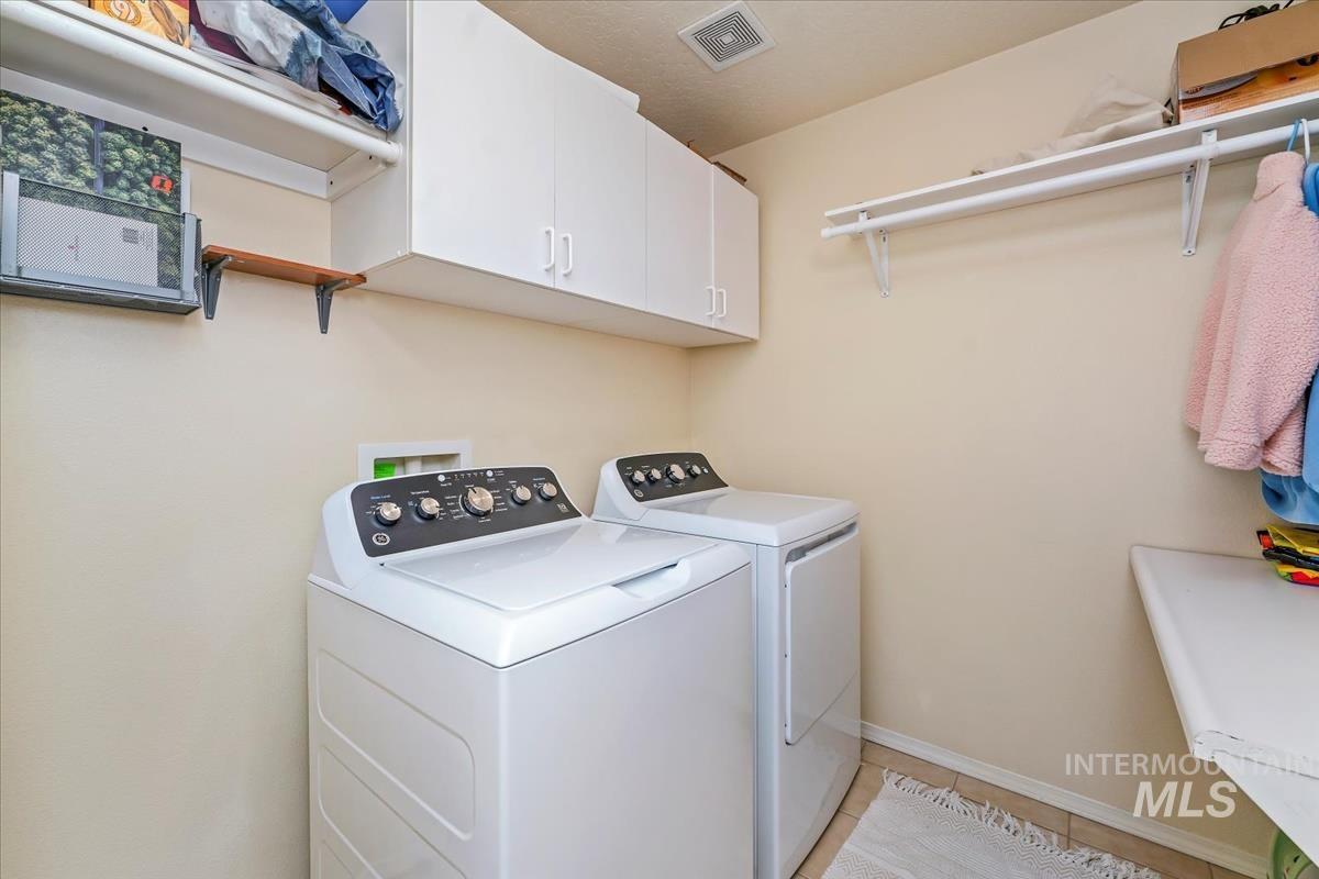 Laundry area with light tile patterned flooring, washer and dryer, and cabinet space