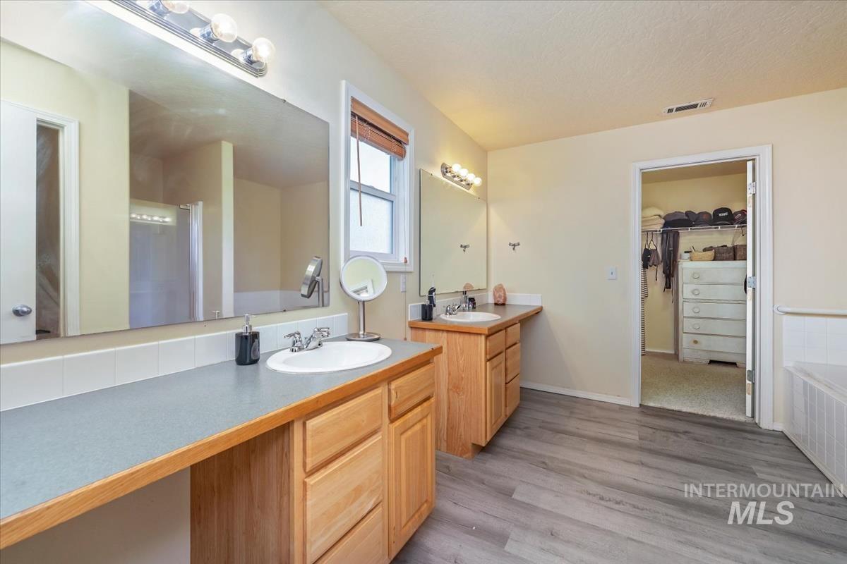 Full bathroom featuring a walk in closet, two vanities, light wood-type flooring, a shower stall, and a bath