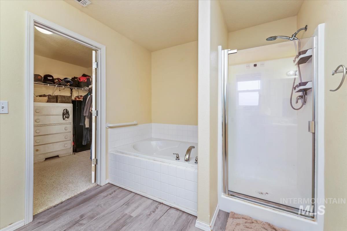 Bathroom with a walk in closet, light wood-type flooring, a stall shower, and a garden tub