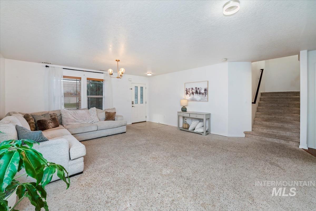Living room with a textured ceiling, stairs, a chandelier, and carpet flooring