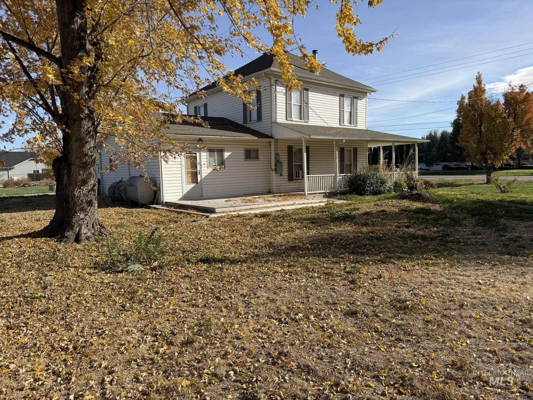 View of front of property with oil tank, a porch, a front lawn, and a shingled roof