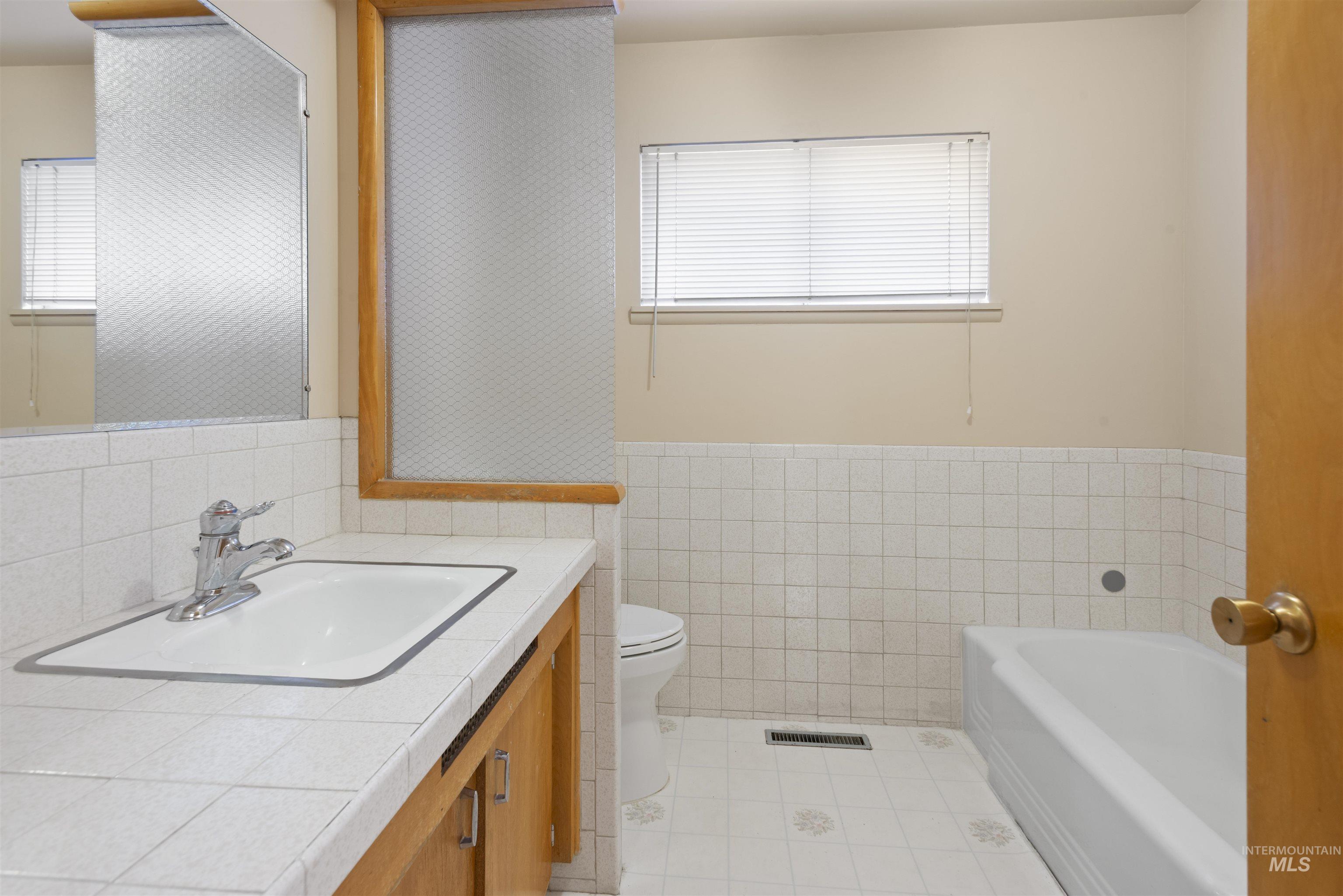 Full bathroom with tile walls, a garden tub, vanity, a wainscoted wall, and light tile patterned floors