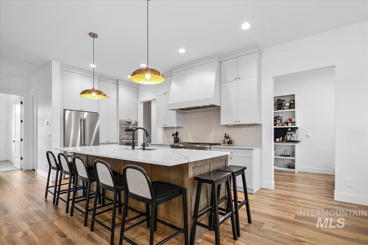 Kitchen with a kitchen breakfast bar, white cabinets, an island with sink, tasteful backsplash, and light wood-type flooring