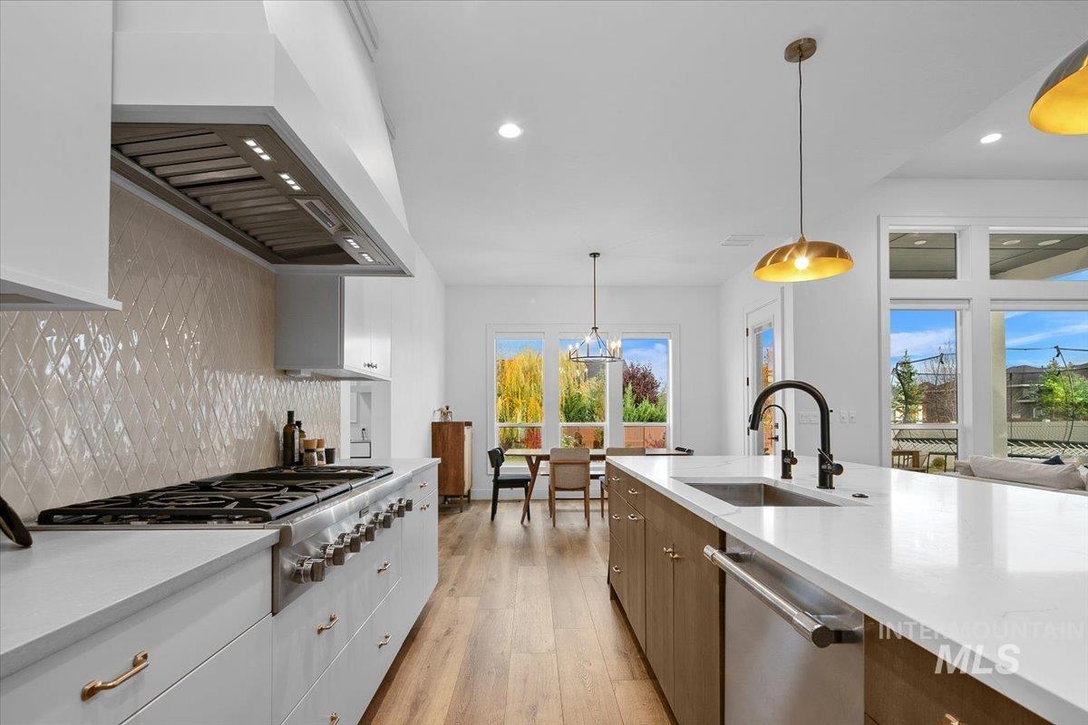 Kitchen with decorative backsplash, hanging light fixtures, custom range hood, white cabinets, and recessed lighting
