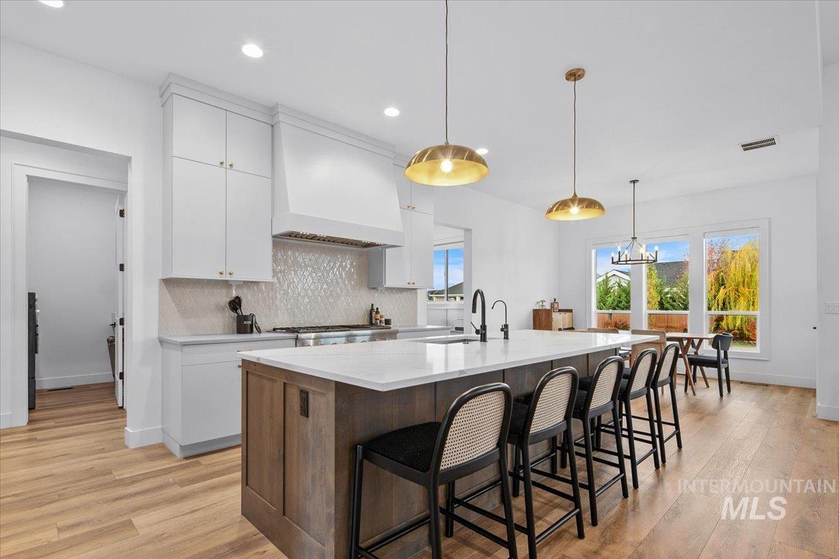 Kitchen featuring white cabinets, a kitchen breakfast bar, backsplash, hanging light fixtures, and a kitchen island with sink