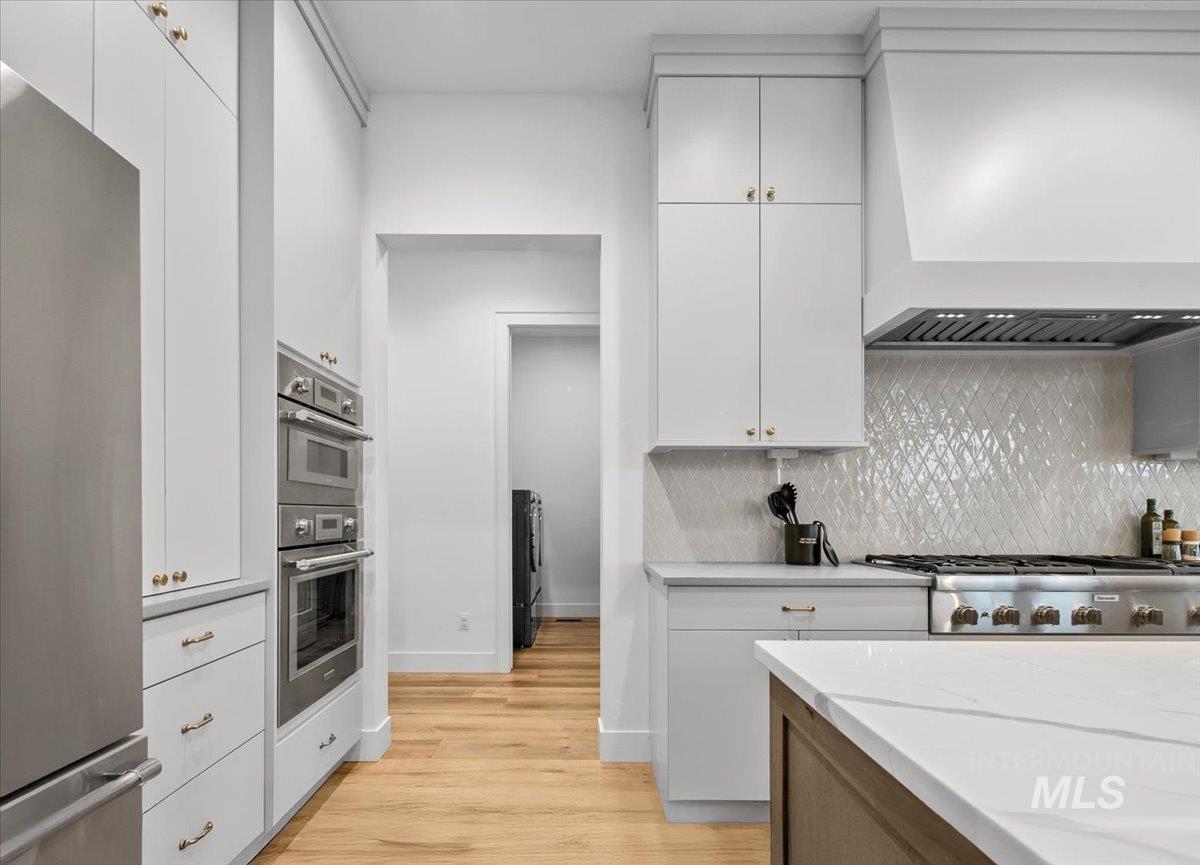 Kitchen with premium range hood, appliances with stainless steel finishes, white cabinetry, and light wood-style floors