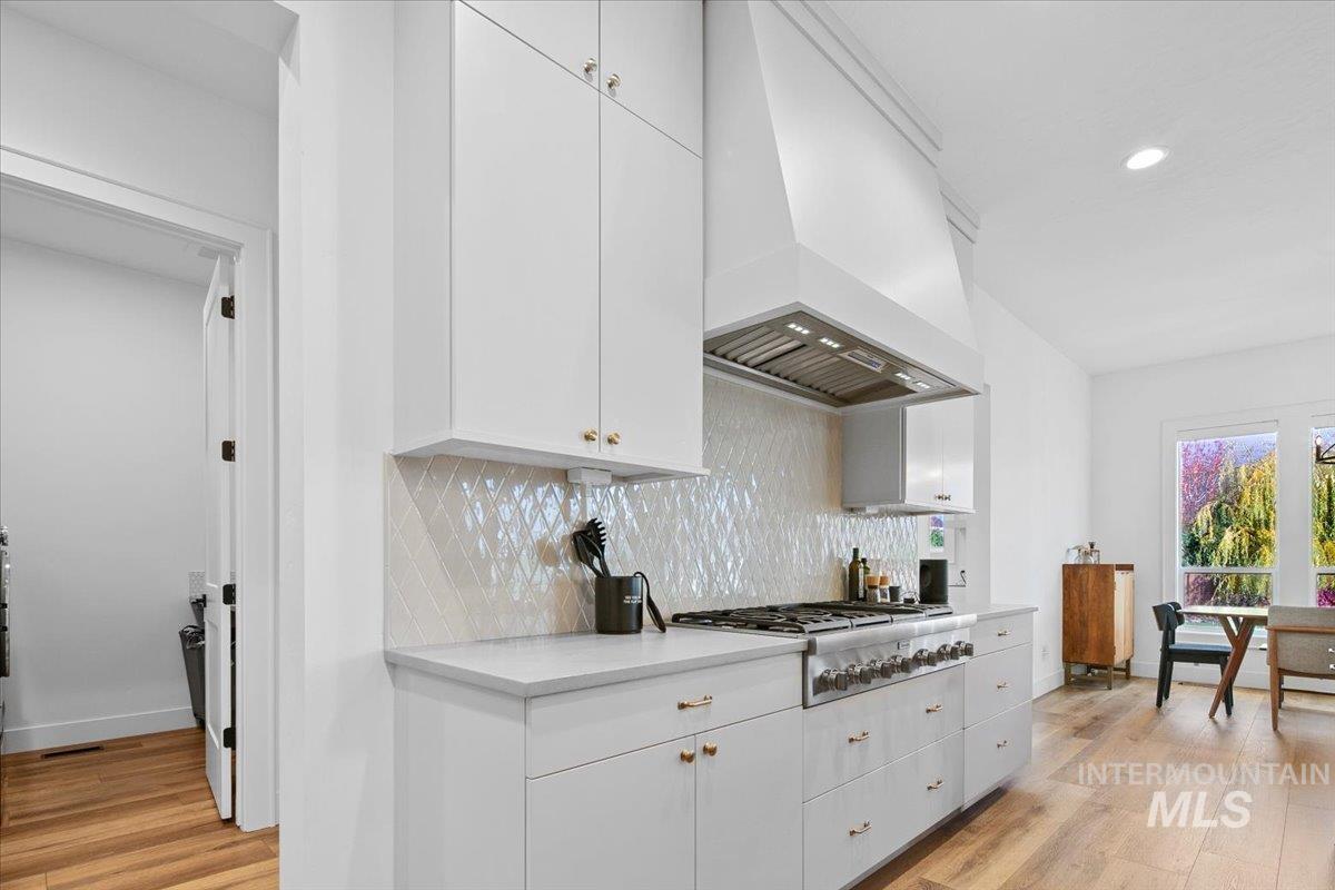 Kitchen with backsplash, light wood-style floors, custom exhaust hood, white cabinetry, and stainless steel gas stovetop