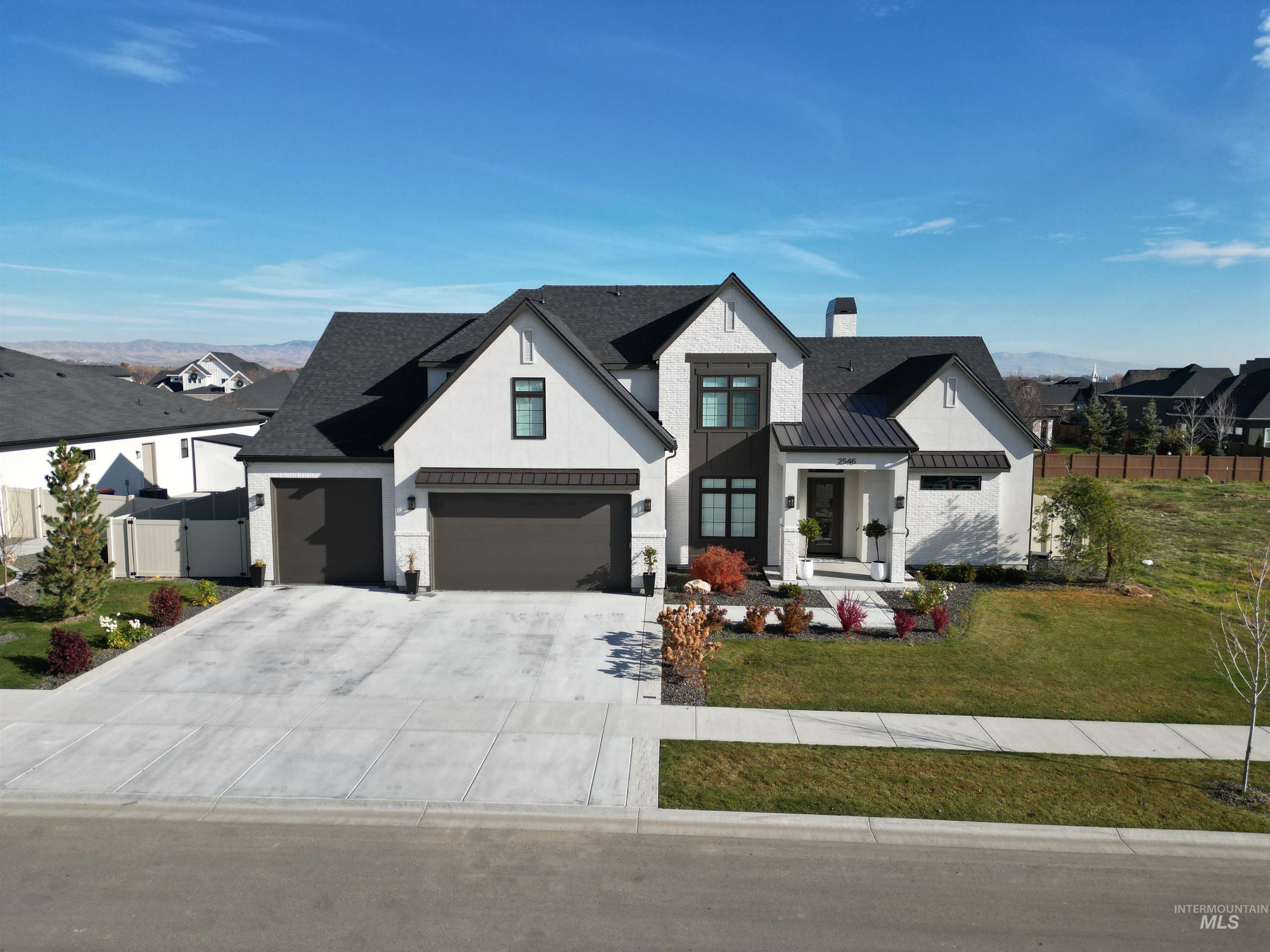 Modern inspired farmhouse featuring a standing seam roof, a metal roof, concrete driveway, a chimney, and stucco siding