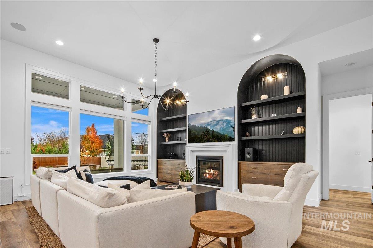 Living room with light wood-style flooring, built in shelves, a glass covered fireplace, recessed lighting, and a chandelier