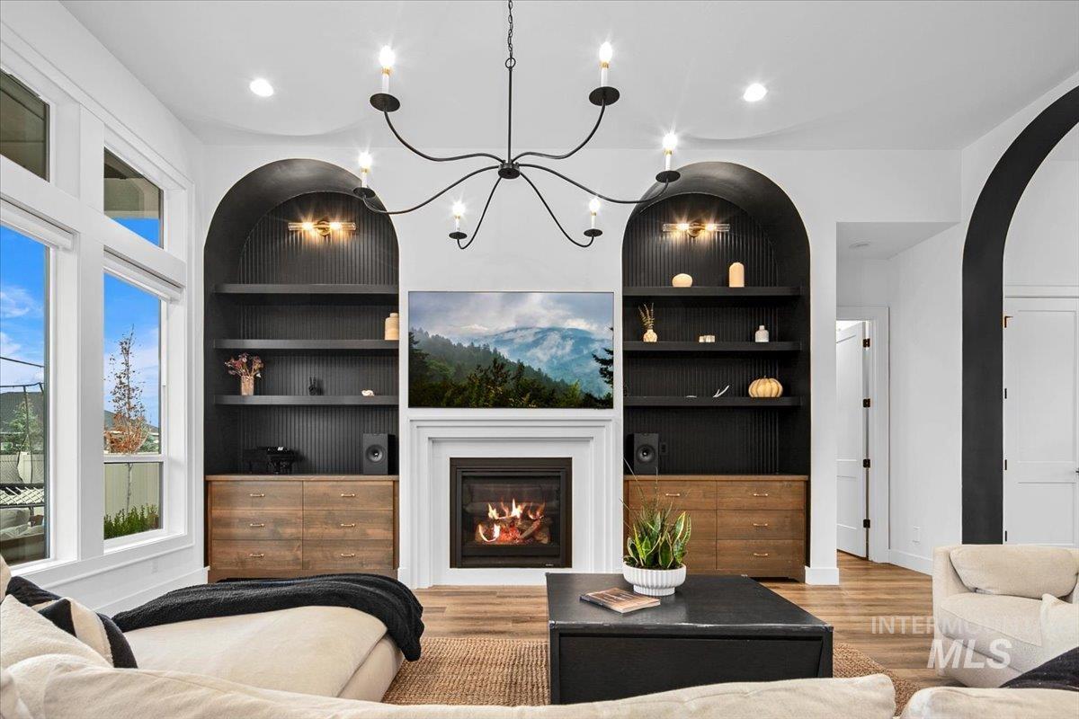Living room with built in features, a glass covered fireplace, light wood-type flooring, recessed lighting, and arched walkways