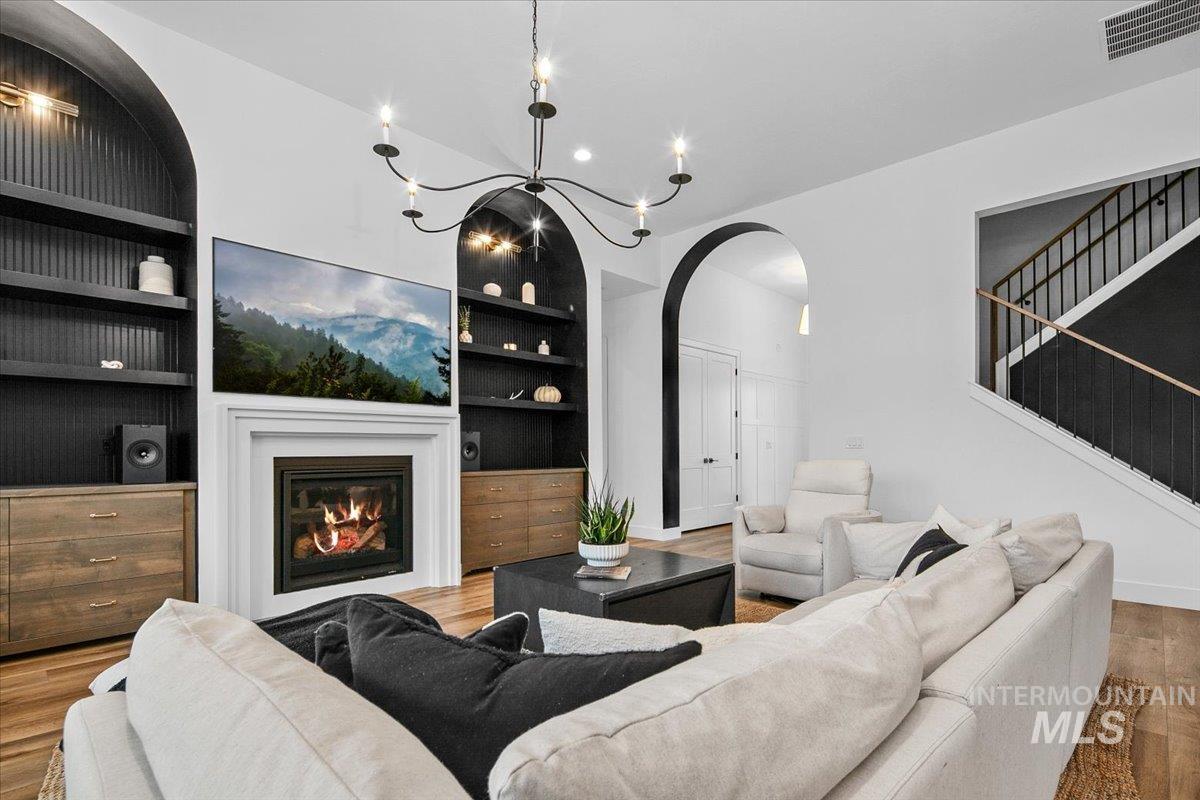 Living area with built in shelves, wood finished floors, a glass covered fireplace, a chandelier, and recessed lighting