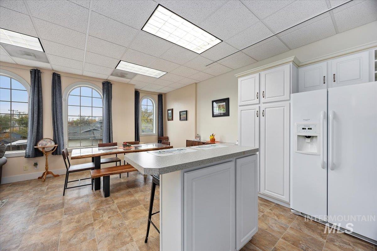 Kitchen with white refrigerator with ice dispenser, a drop ceiling, a breakfast bar area, white cabinetry, and a kitchen island