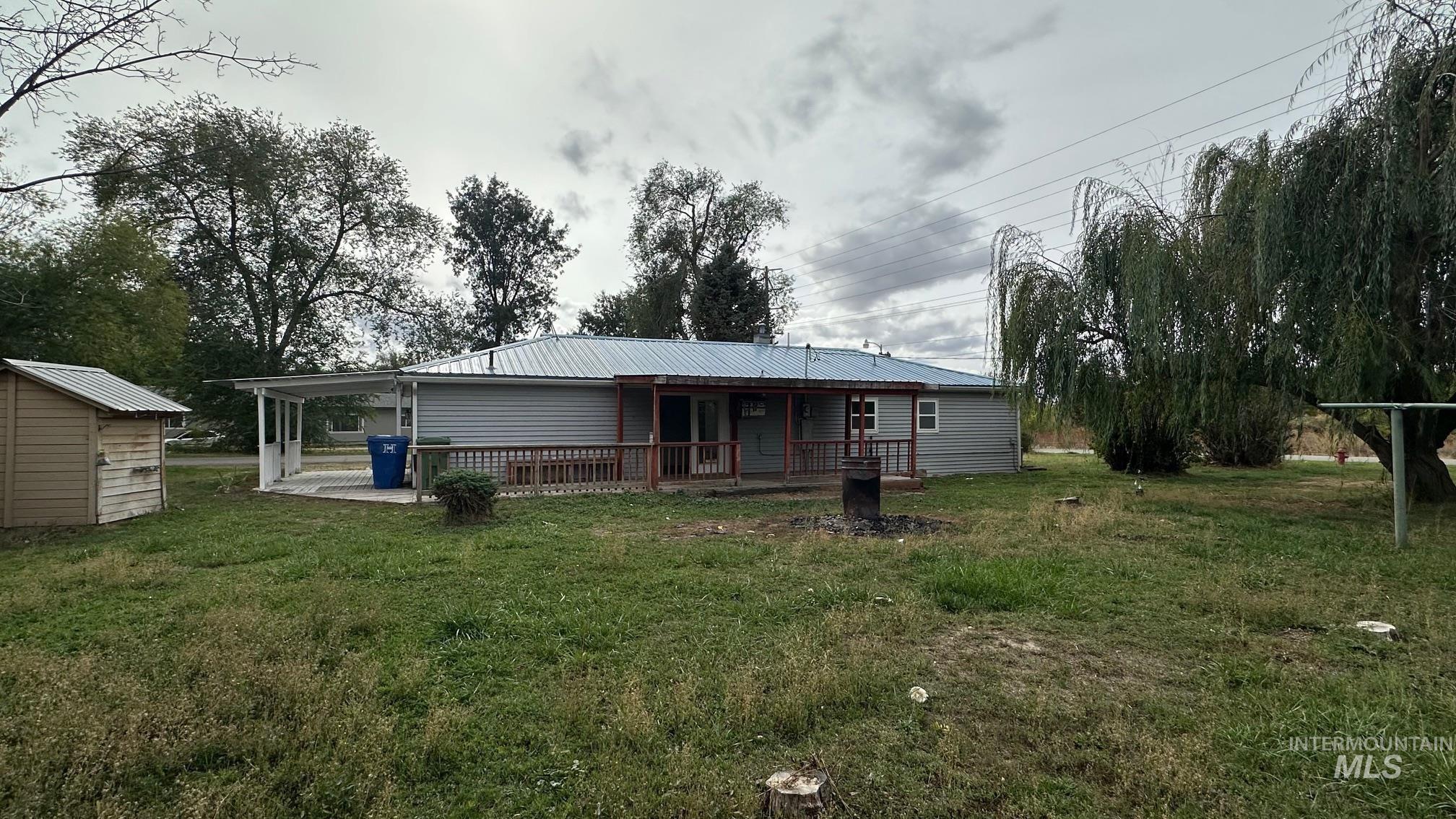 Rear view of house featuring a lawn, a metal roof, an attached carport, a storage shed, and a deck