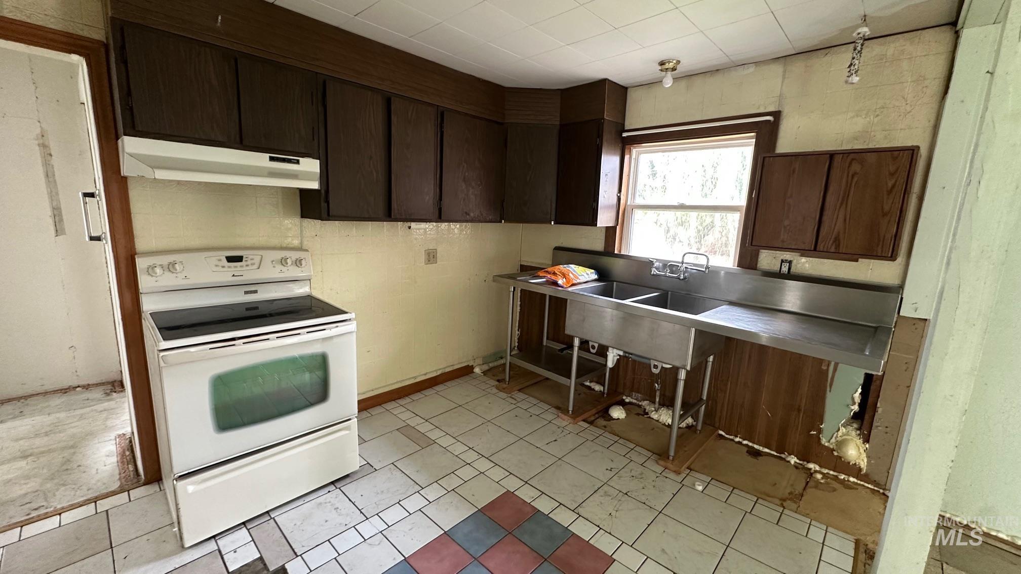 Kitchen with dark brown cabinetry, white electric range, under cabinet range hood, and light tile patterned flooring